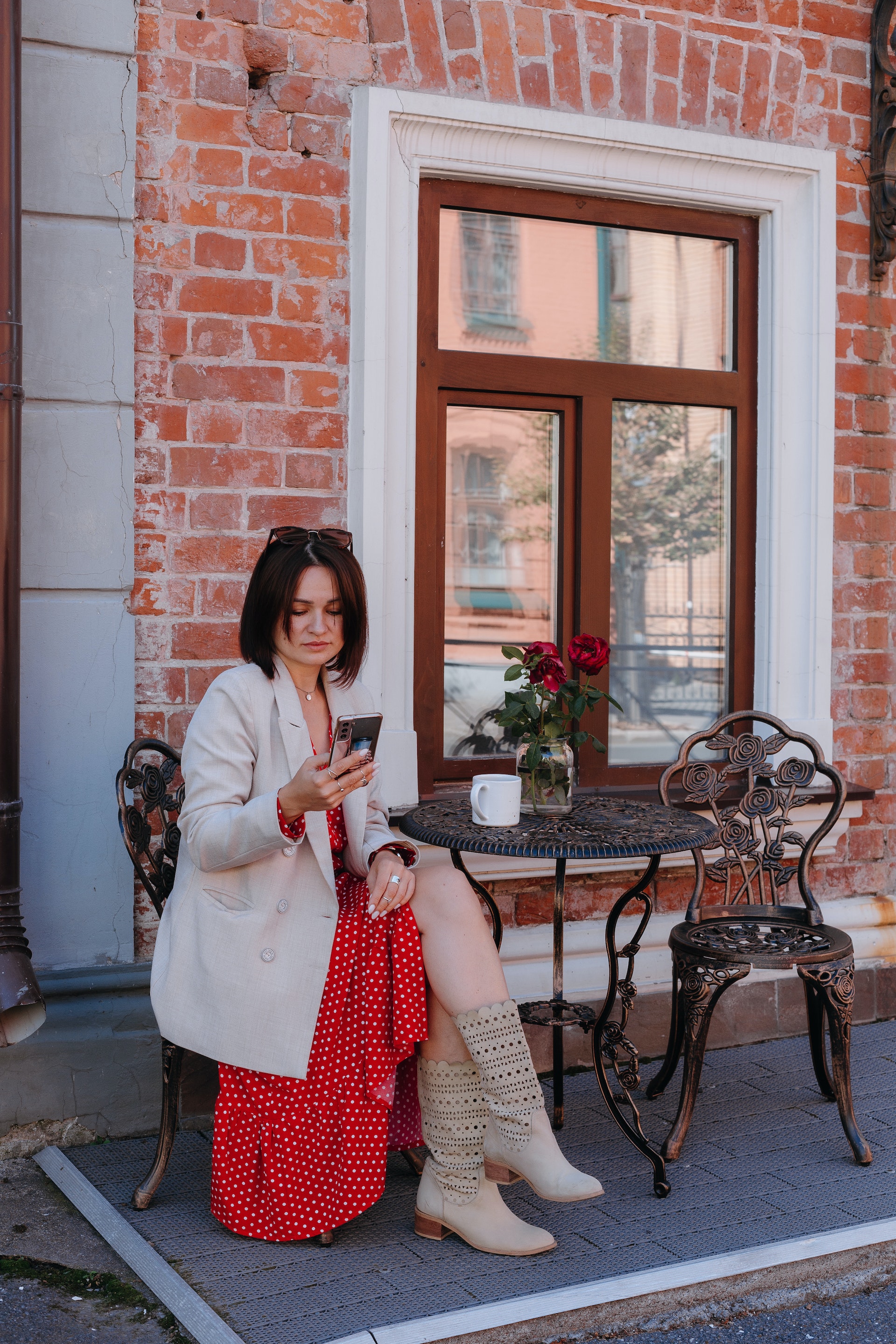 Une femme assise à un café sur le trottoir tout en consultant son téléphone portable | Source : Pexels