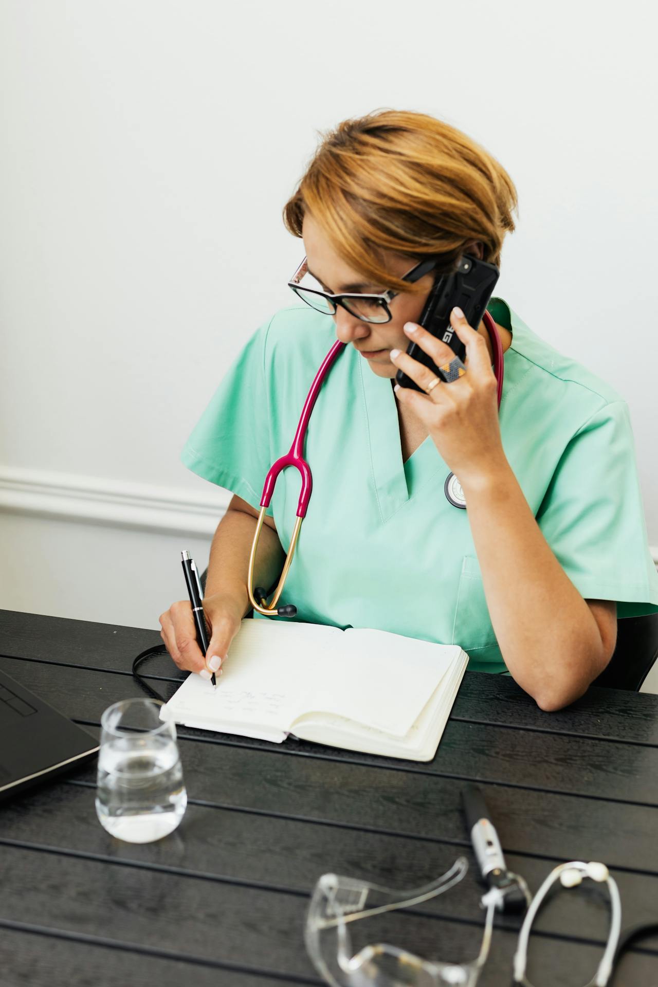 Un membre du personnel médical parle au téléphone tout en écrivant sur un cahier | Source : Pexels