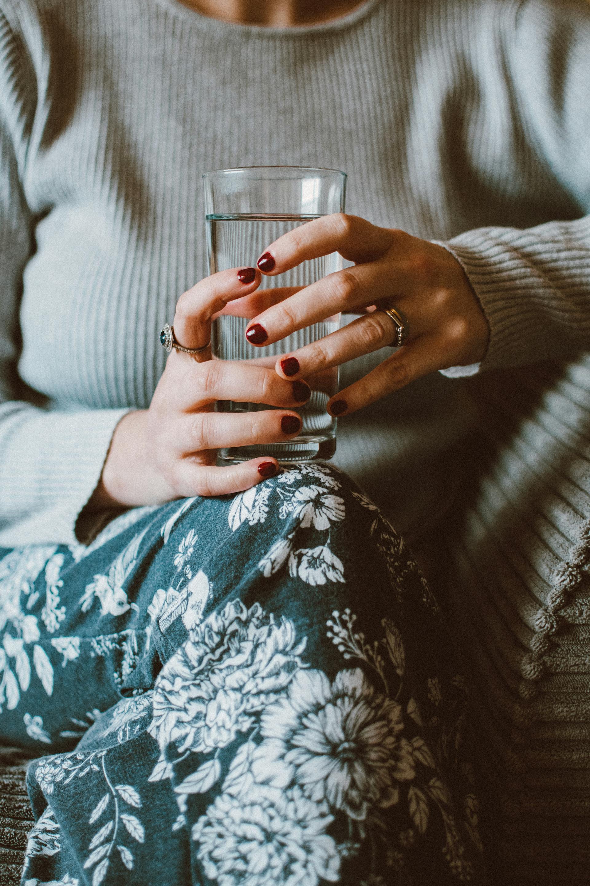 Une femme assise sur un canapé tout en tenant un verre d'eau | Source : Pexels