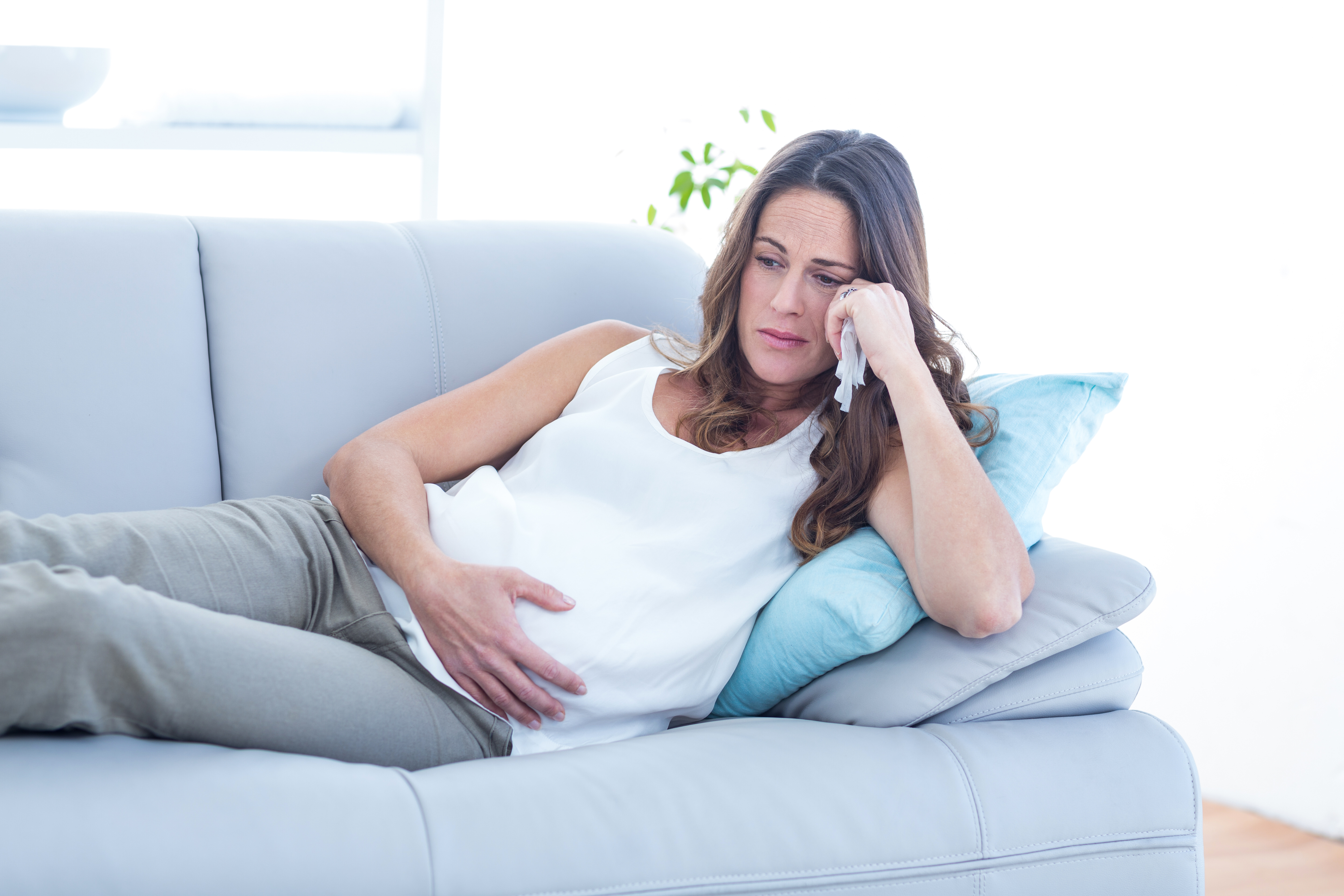 Une femme enceinte assise sur un canapé, l'air triste | Source : Shutterstock