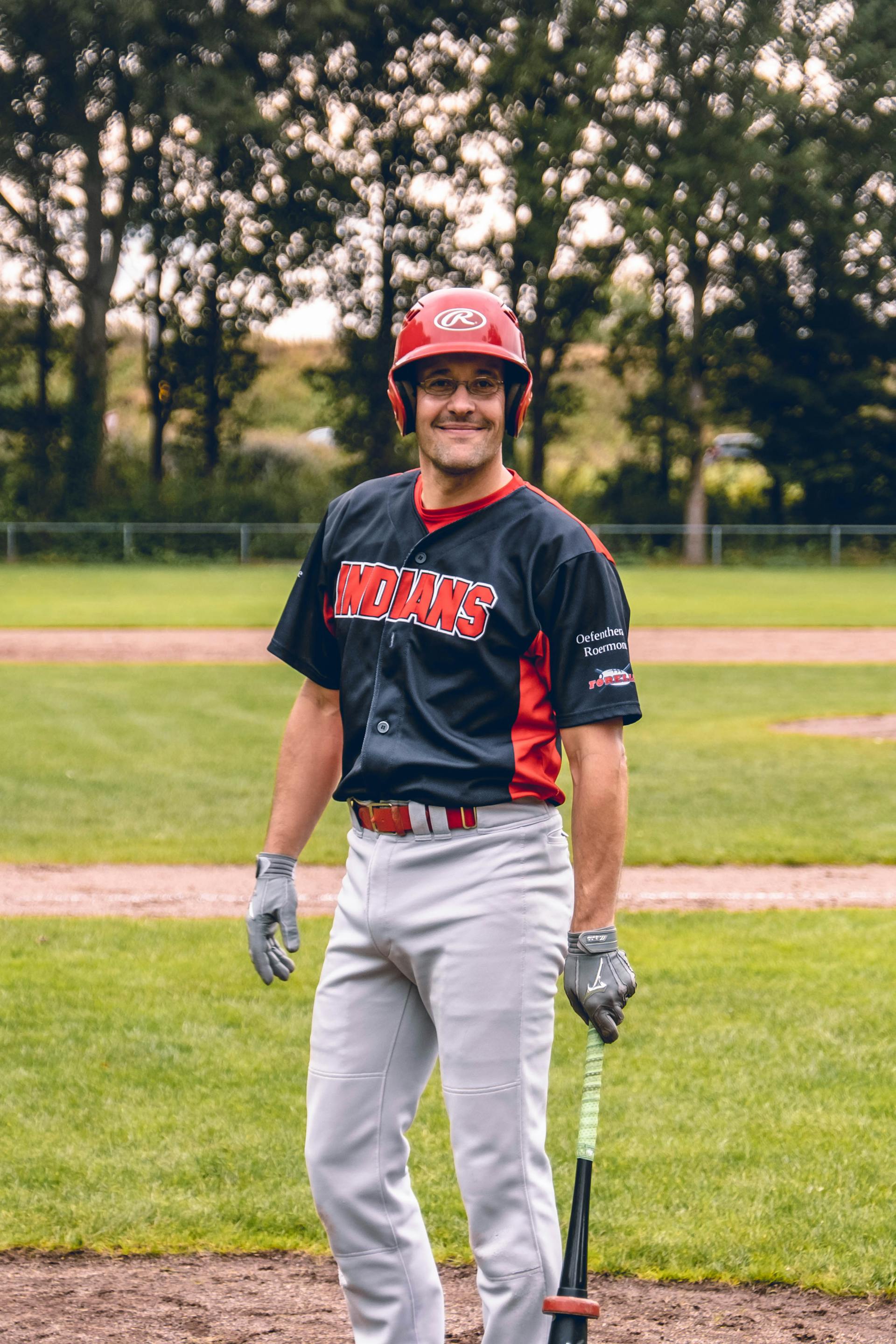 Un homme en uniforme de baseball debout et souriant à l'extérieur | Source : Pexels