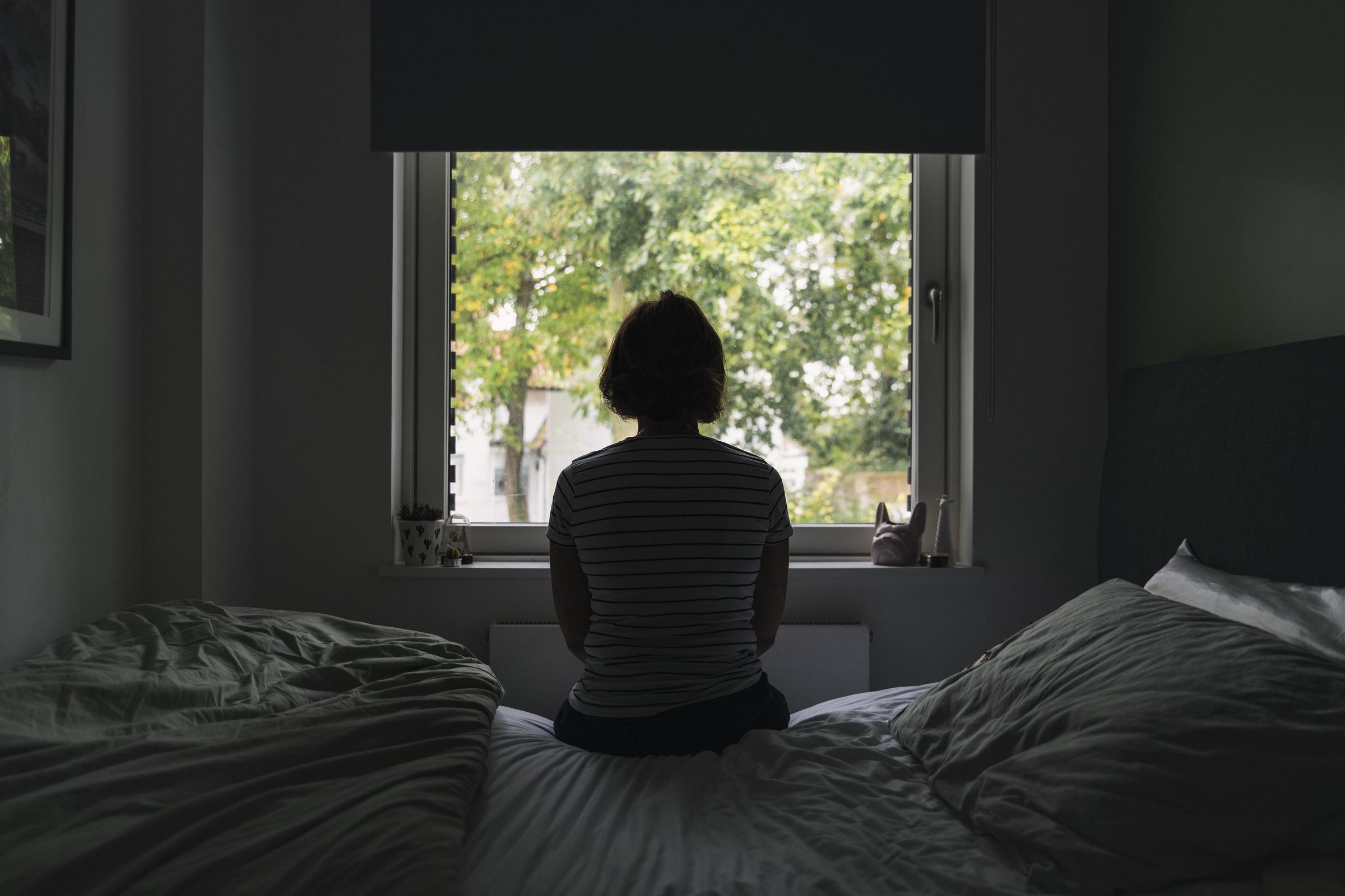 Une femme regardant par la fenêtre dans sa chambre | Source : Getty Images