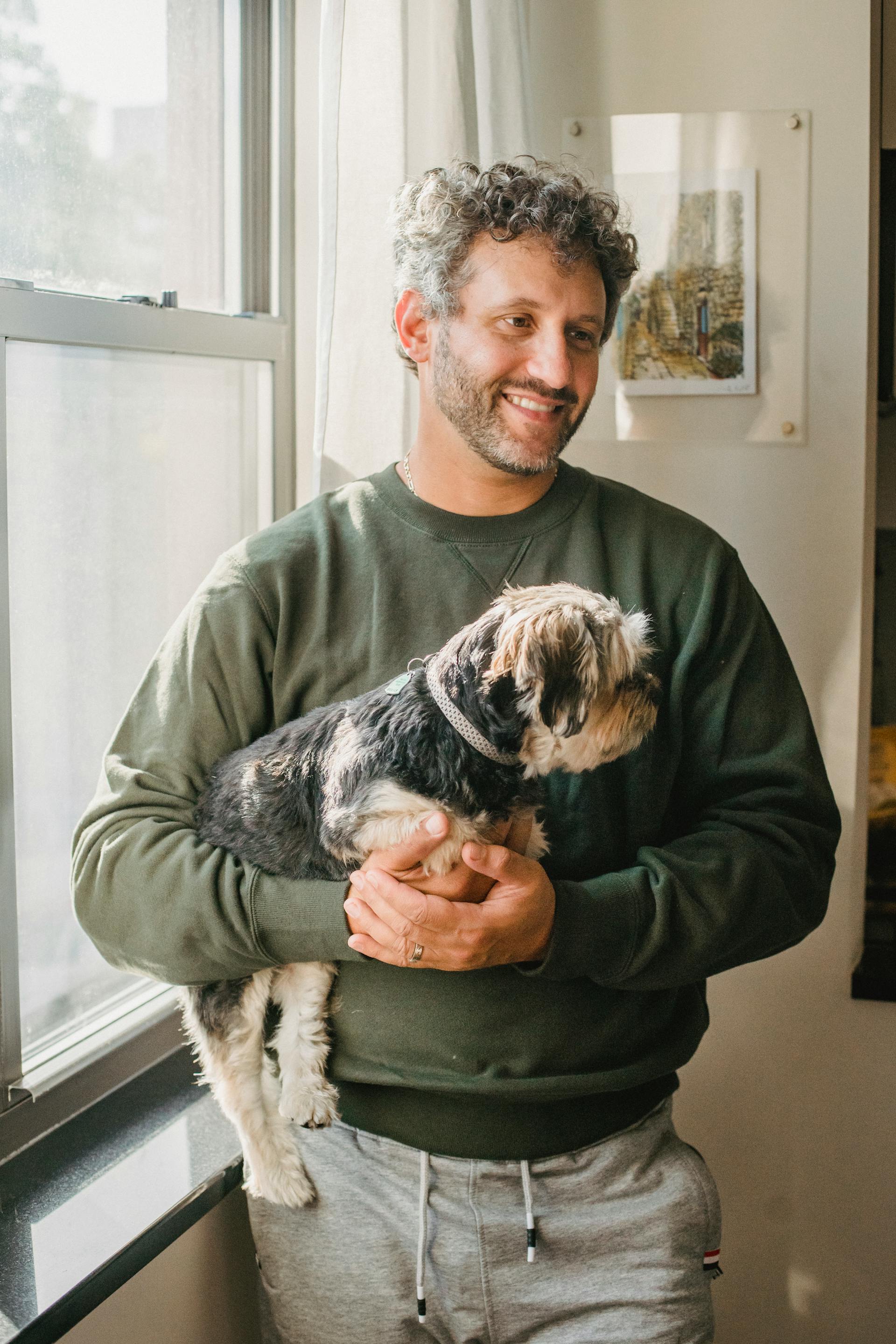 Ein Mann hält einen Hund, während er neben einem Fenster steht | Quelle: Pexels