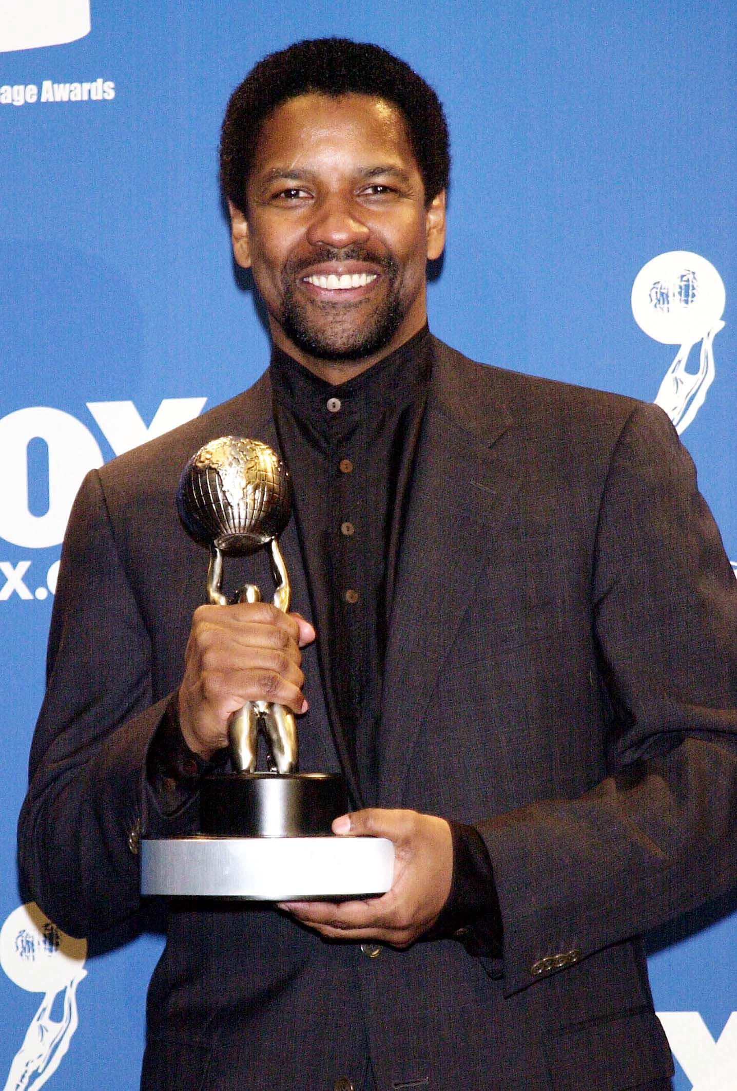 Denzel Washington sourit en tenant son NAACP Image Award pour « The Hurricane ». Sa barbichette bien dessinée et sa coupe de cheveux mi-longue donnent une image mature et raffinée de l'acteur alors qu'il entre dans une nouvelle phase de gloire.