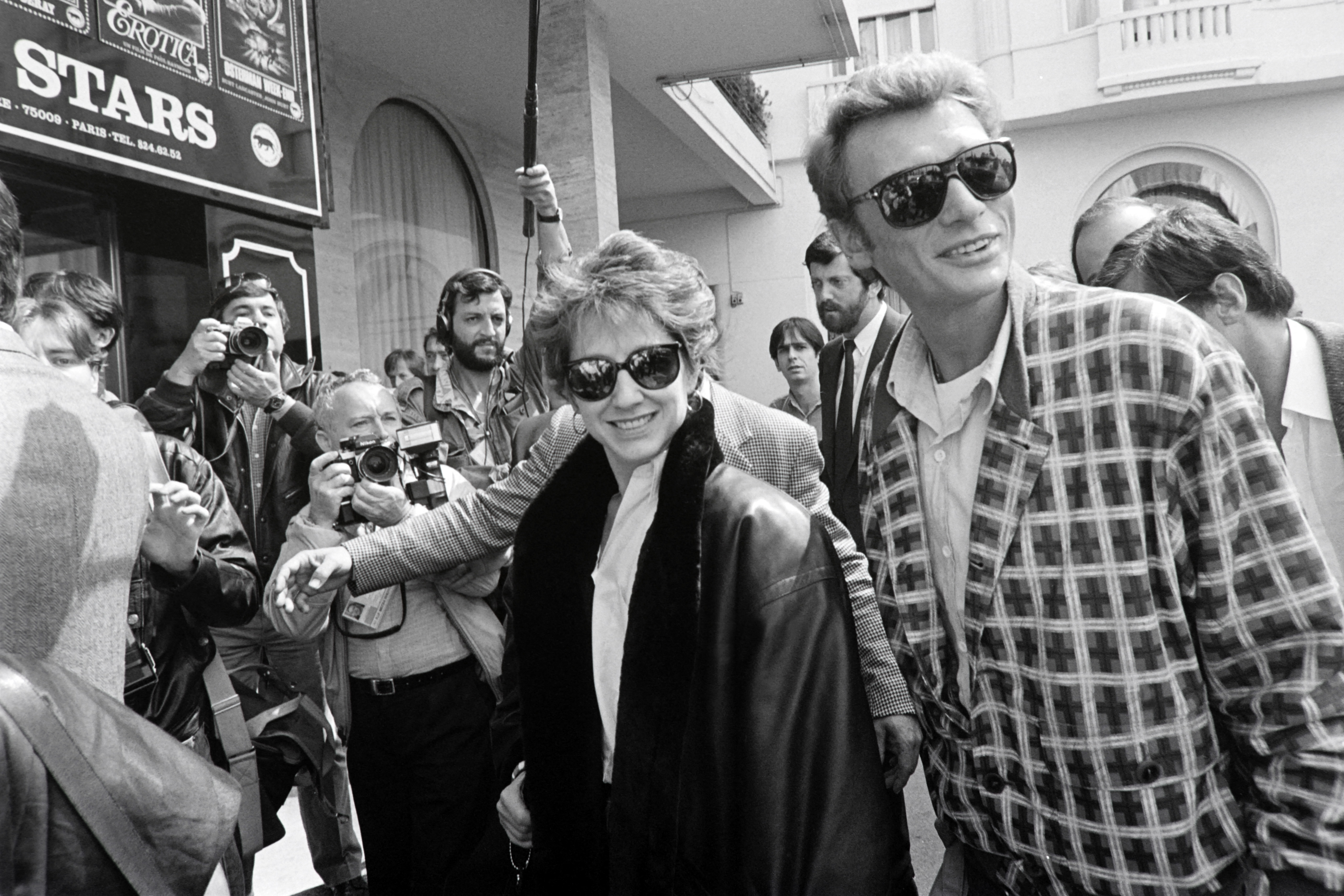 L'actrice française Nathalie Baye (au centre) et son compagnon, le chanteur et acteur Johnny Hallyday (à droite), arrivent à l'hôtel Majestic pour assister à la projection du film « Détective », dans lequel ils ont joué sous la direction de Jean-Luc Godard, lors du Festival de Cannes, le 10 mai 1985 I Source : Getty Images