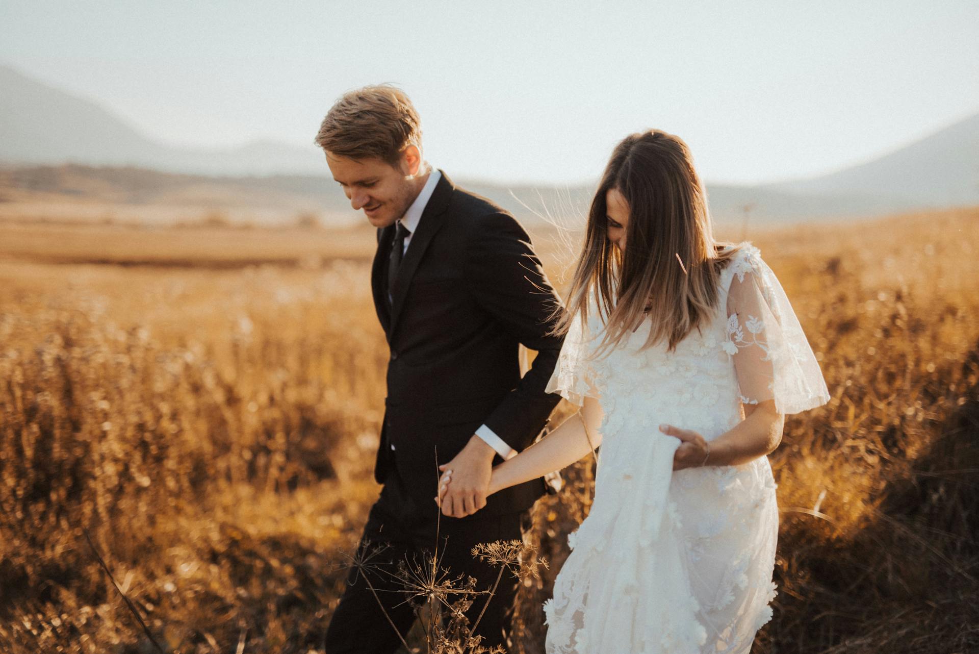 Une mariée et un marié se tenant la main en passant dans un champ | Source : Pexels