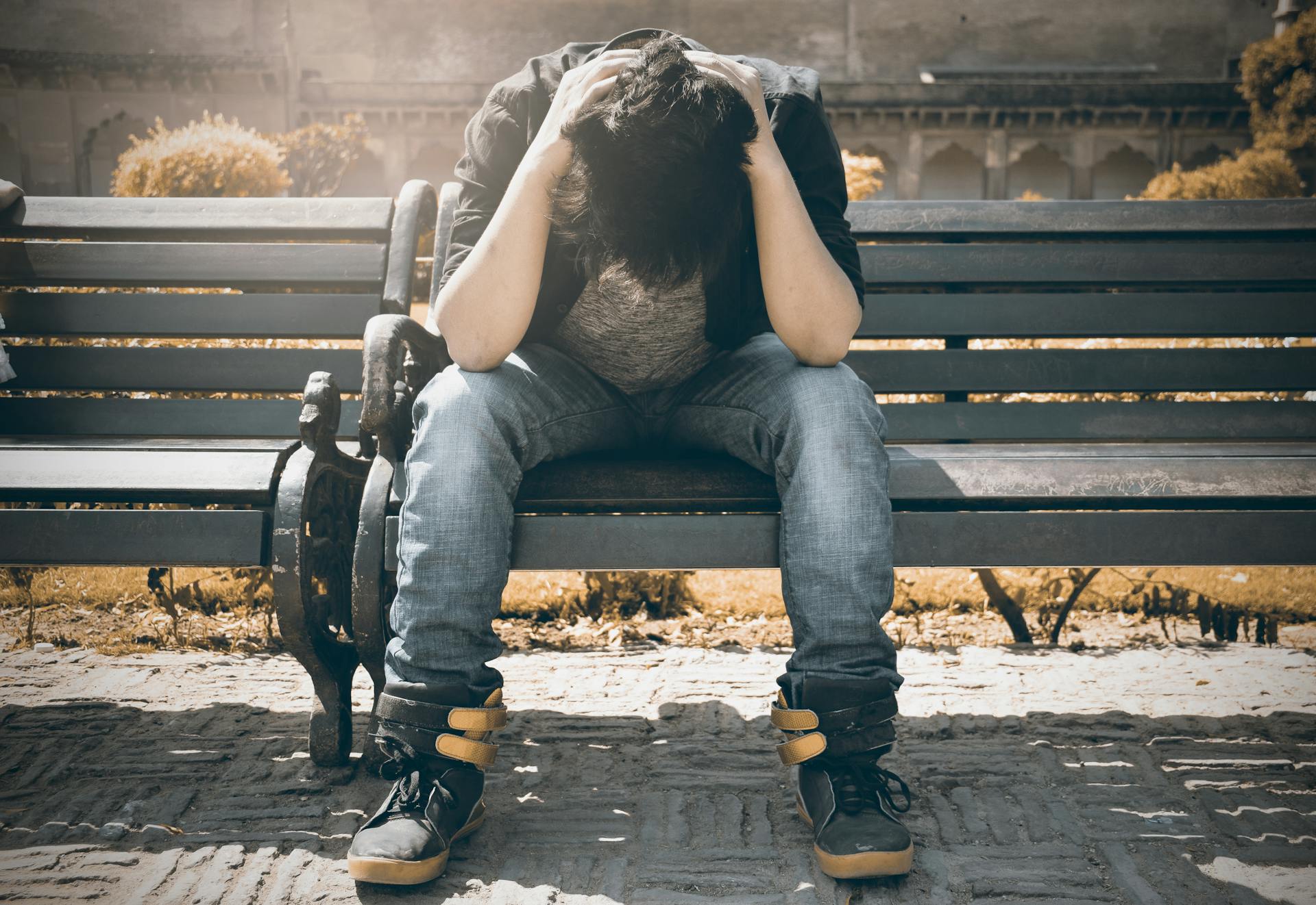 Un homme assis sur un banc, la tête baissée | Source : Pexels