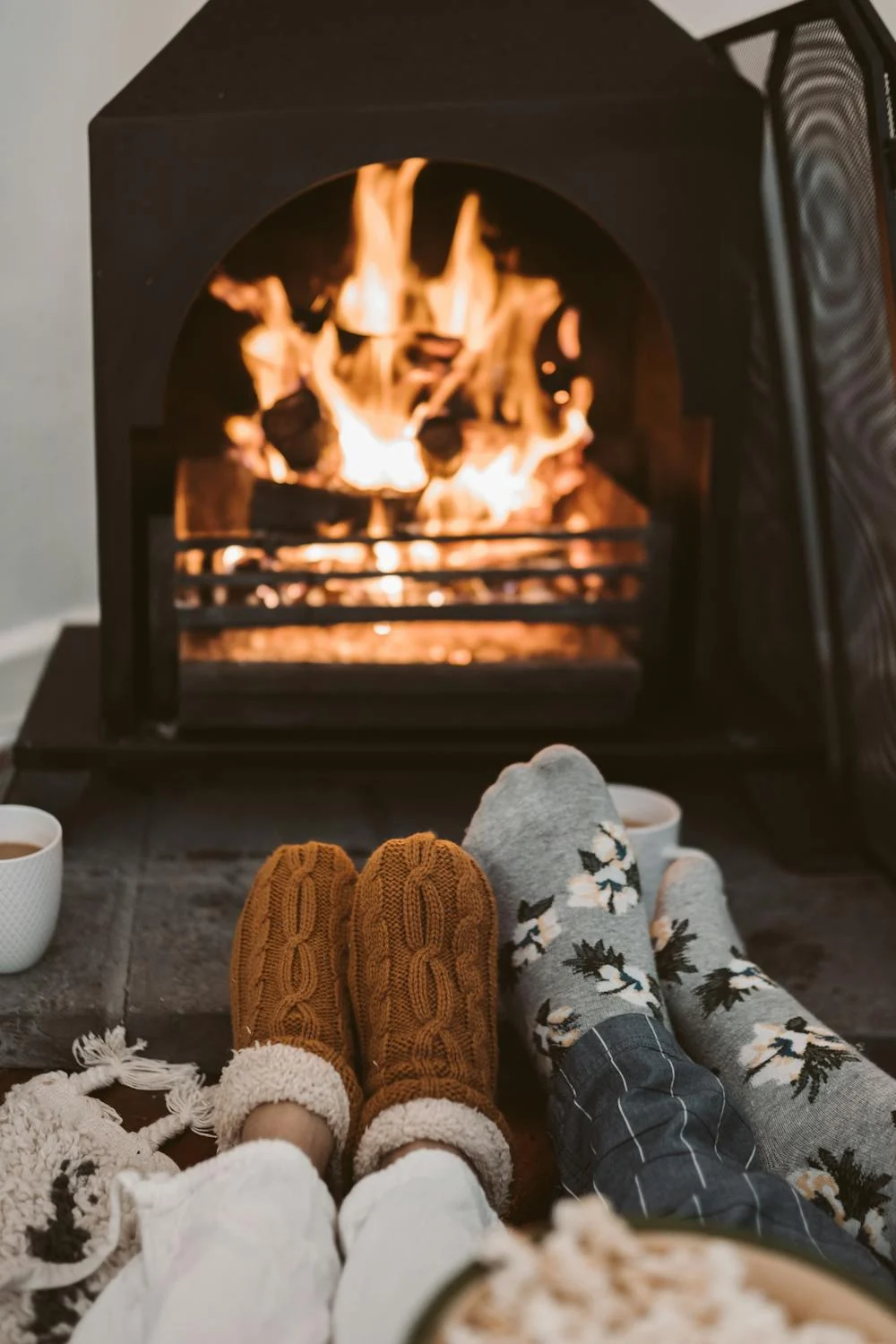 Deux paires de pieds chaussés devant une cheminée rougeoyante | Source : Pexels