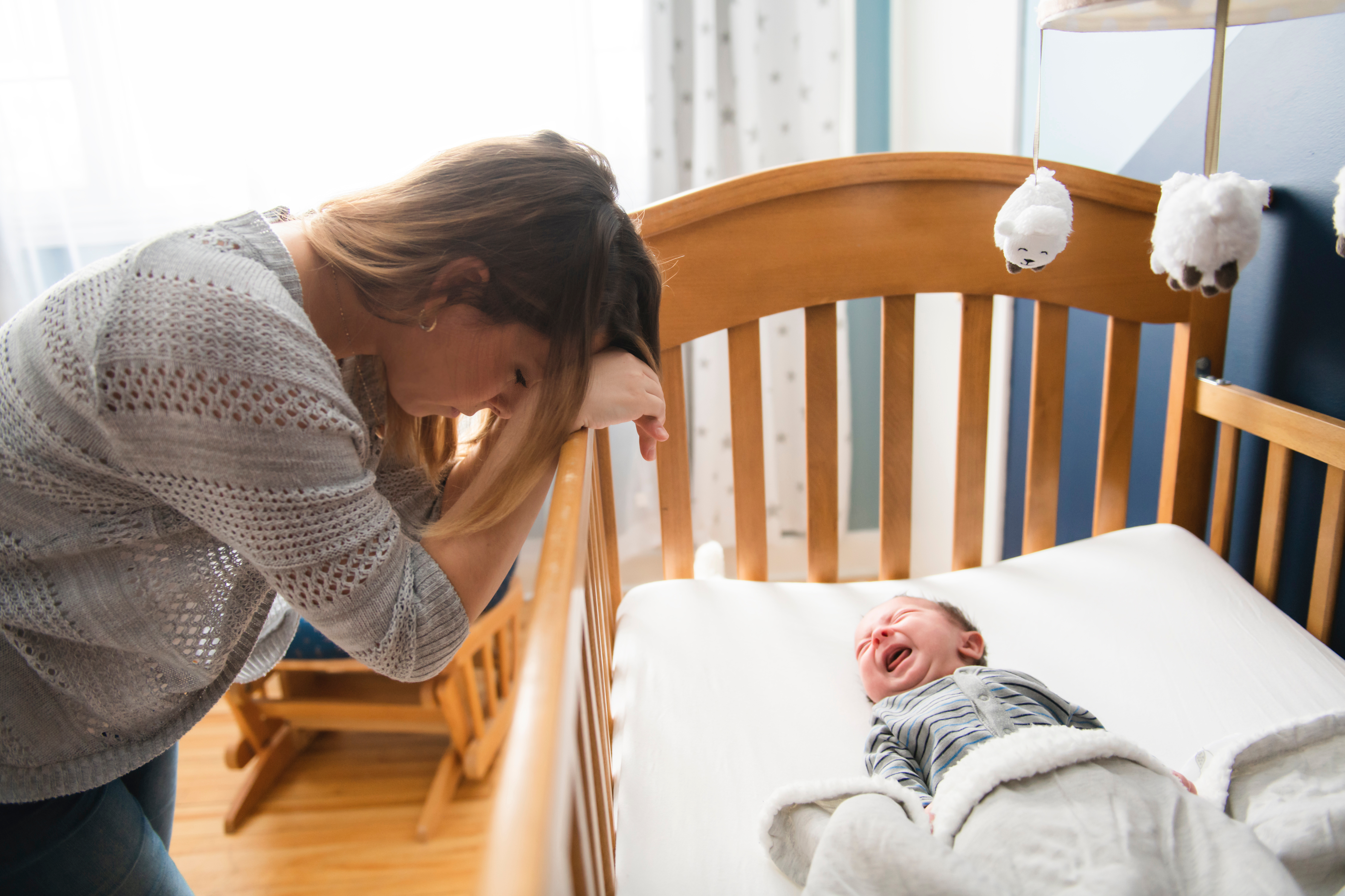 Une mère fatiguée avec un bébé en pleurs couché dans un lit d'enfant | Source : Shutterstock