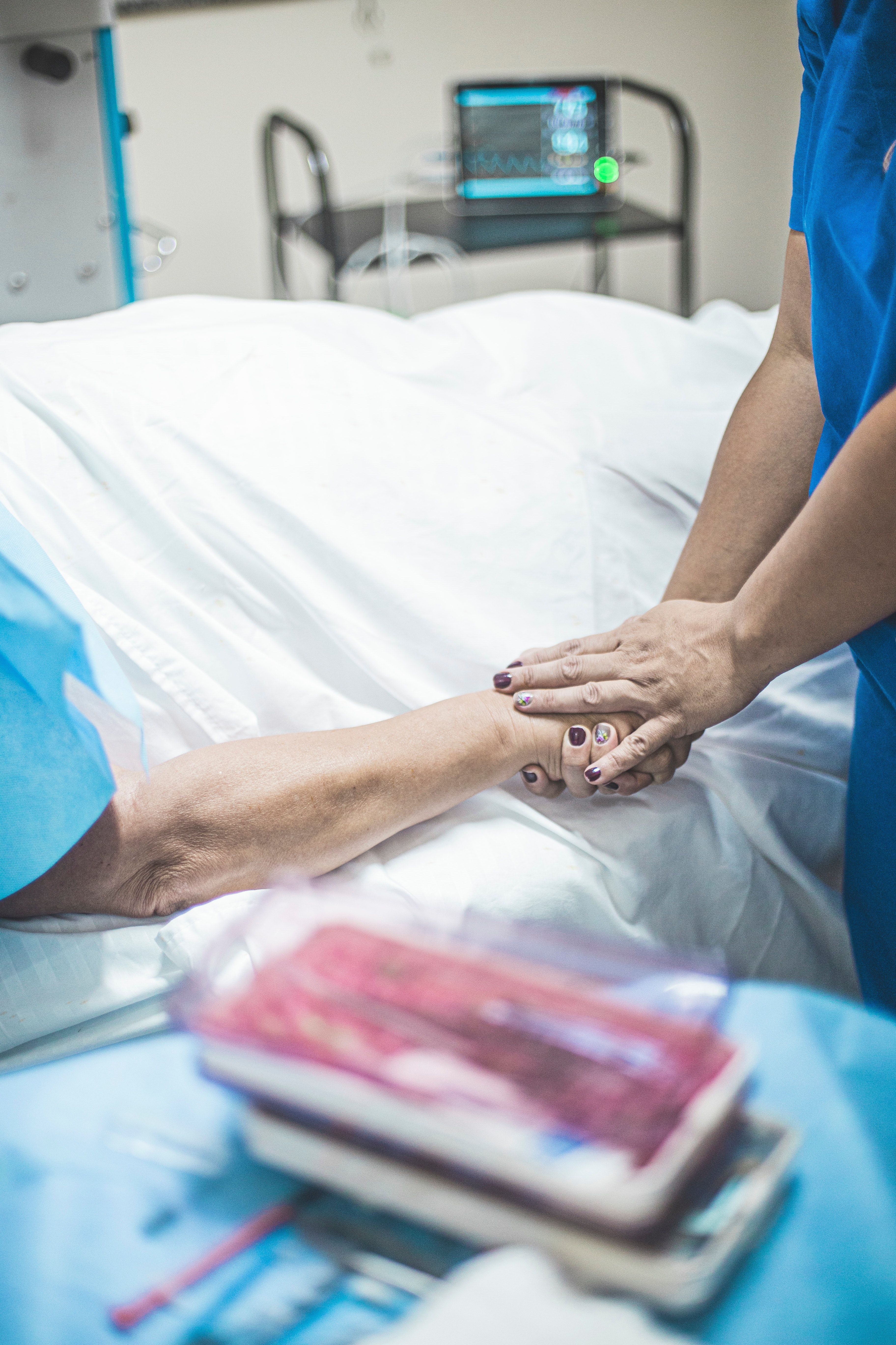 Personne en blouse bleue tenant la main d'un patient allongé sur un lit | Source : Pexels