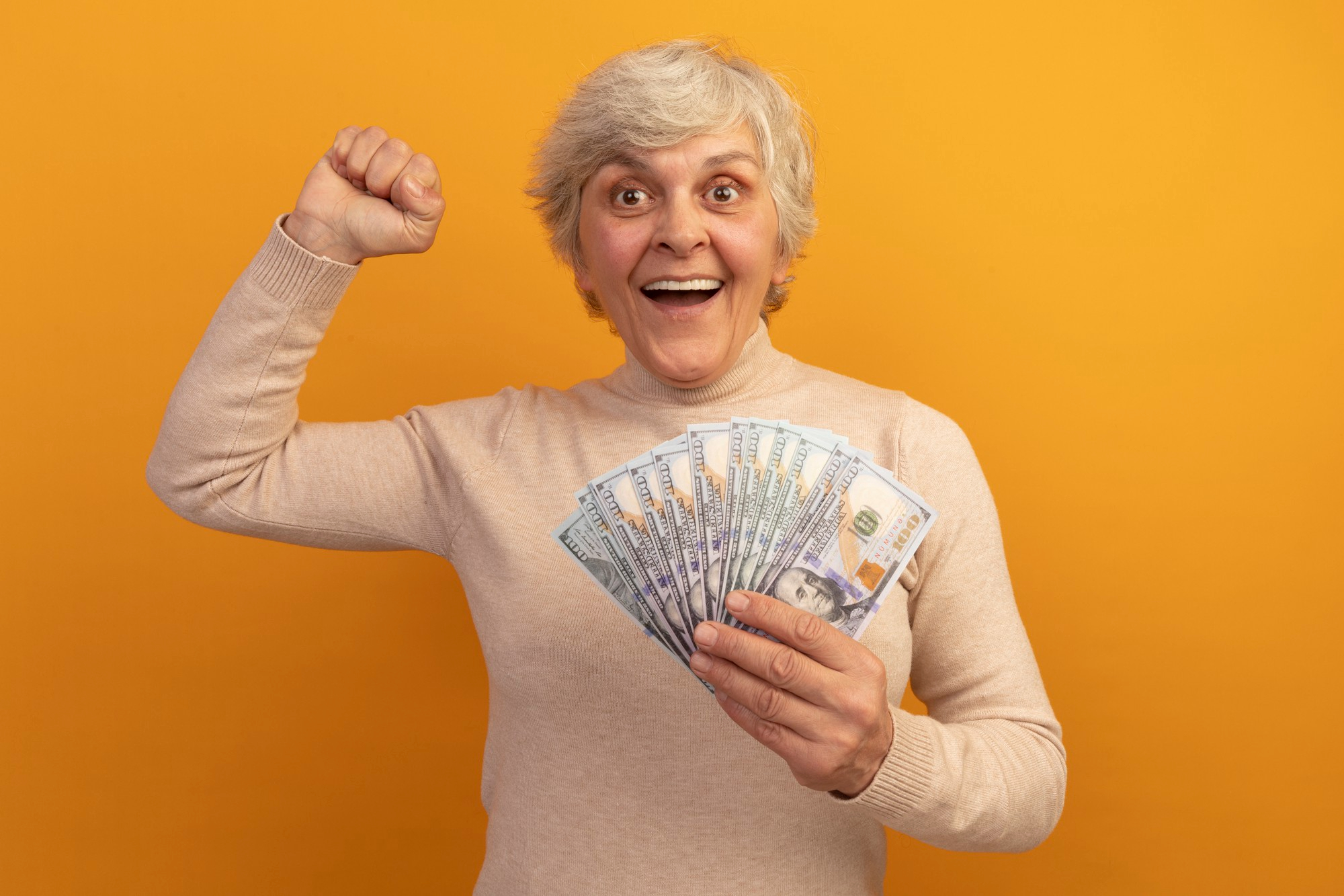 Une femme d'âge moyen fait la fête en tenant de l'argent dans une main | Source : Freepik