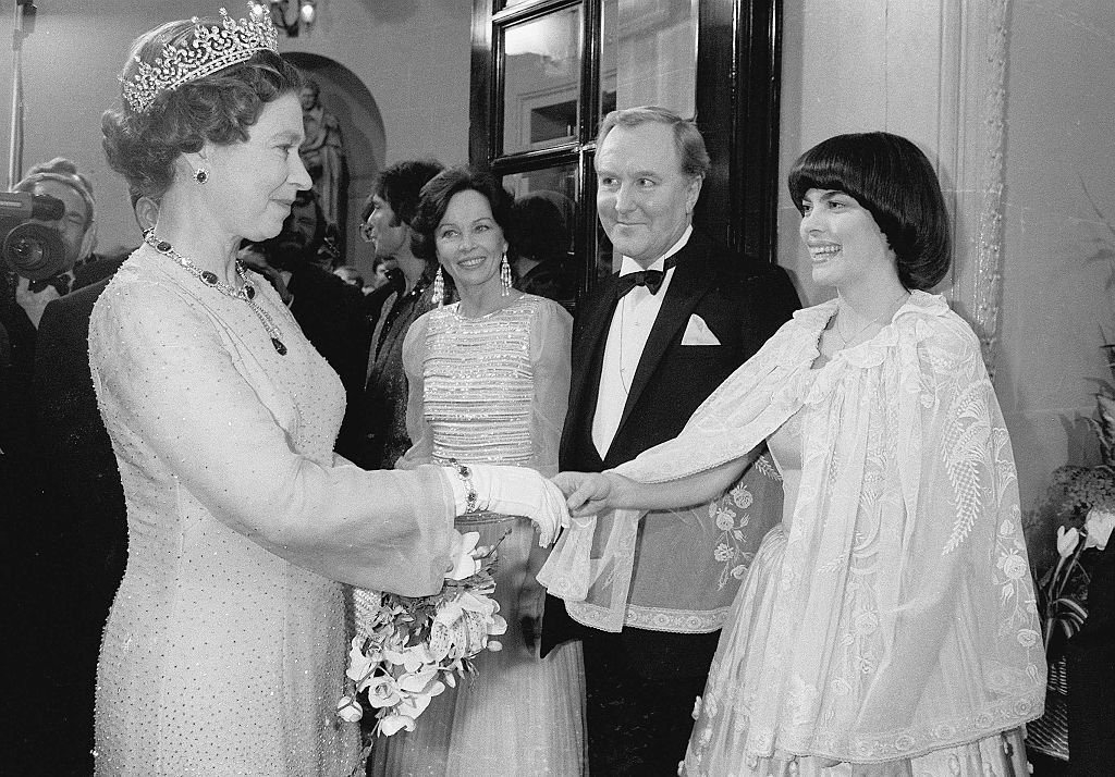 La reine Elisabeth II rencontre la chanteuse française Mireille Mathieu et l'actrice française Leslie Caron à la fin de la représentation royale au Drury Lane Theatre le 23 novembre 1981 à Londres, Angleterre. | Photo : Getty Images