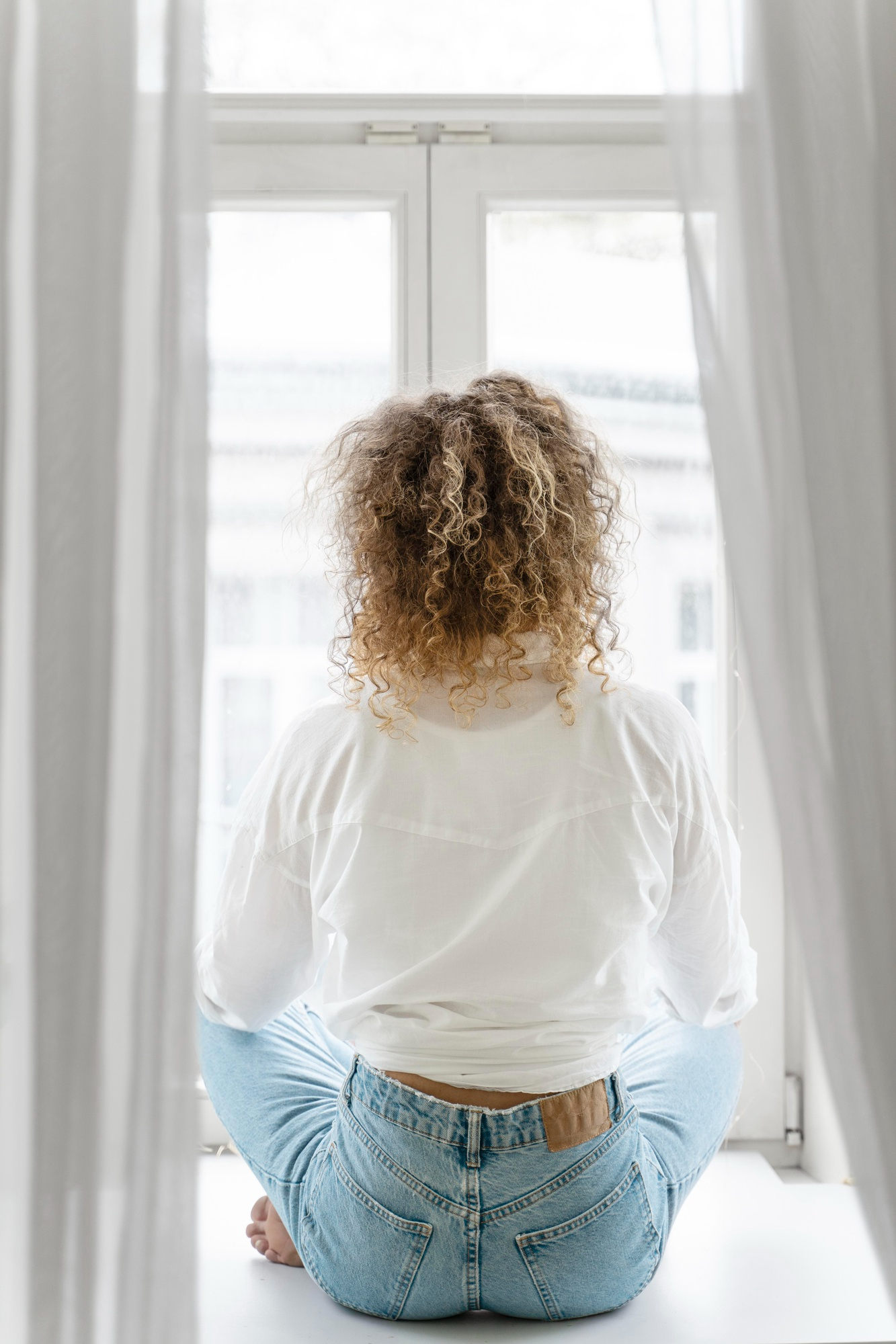 Une femme assise qui regarde à travers une fenêtre | Source : Freepik