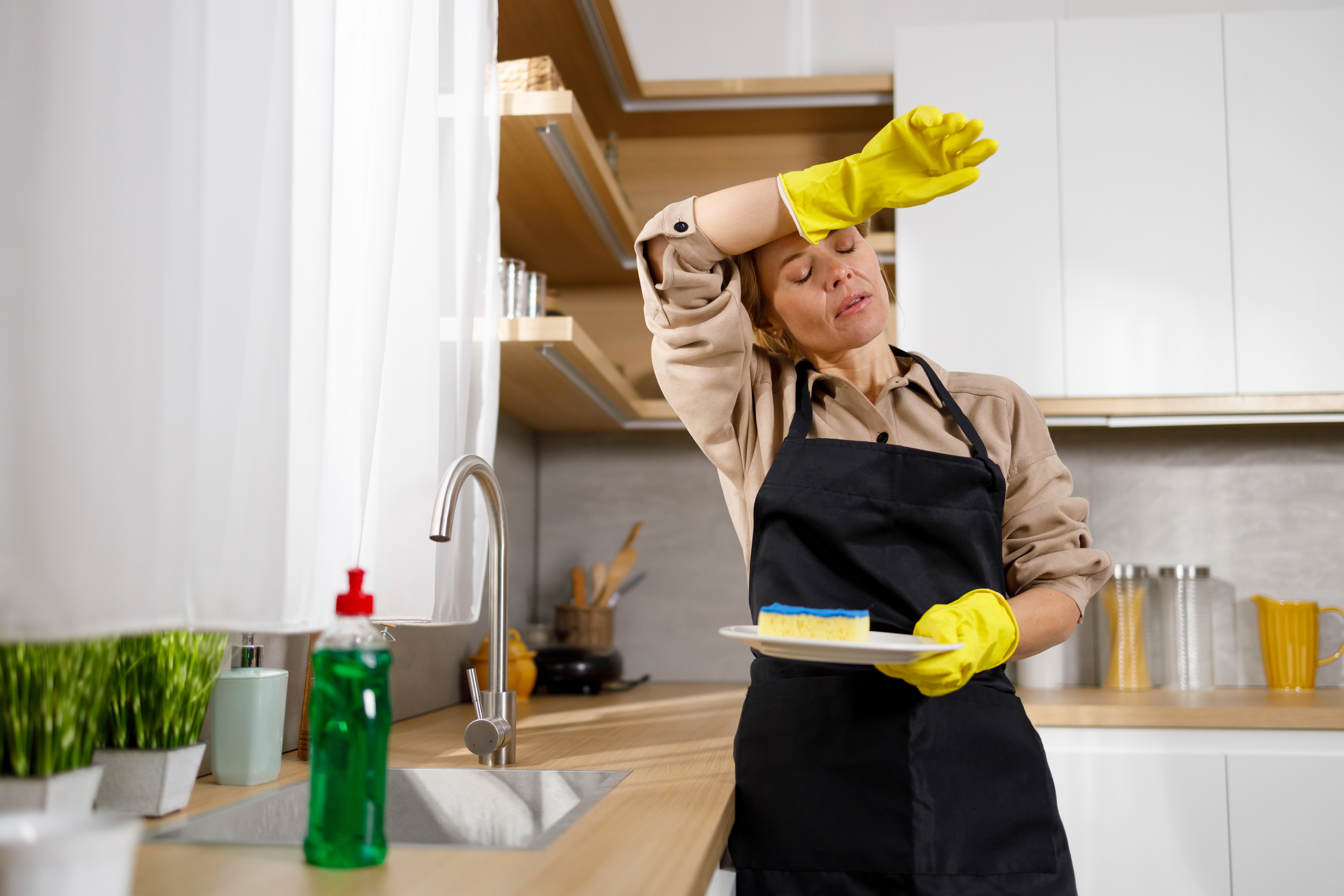 Une femme s'essuie le front en faisant la vaisselle | Source : Shutterstock