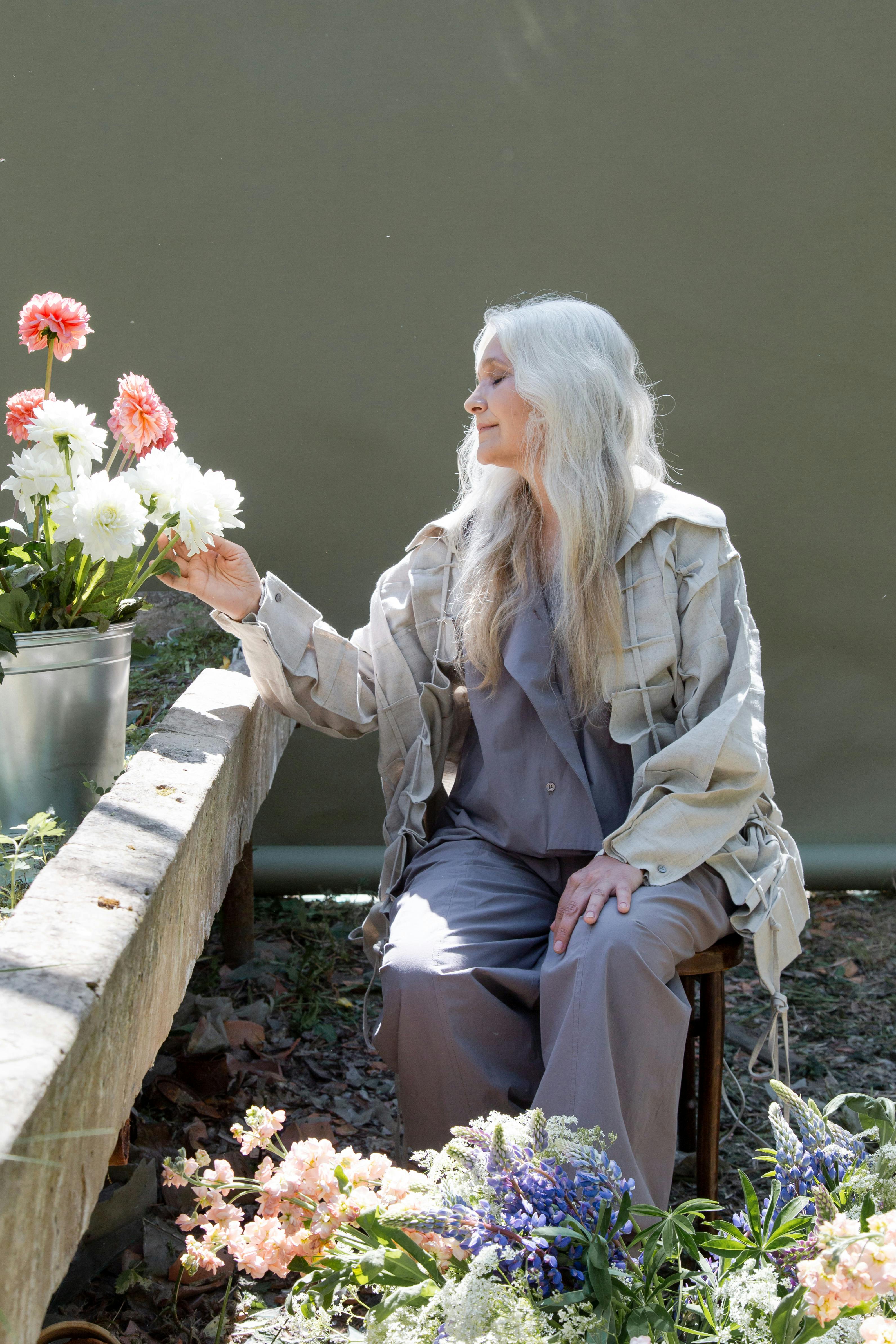 An elderly woman taking a photo with flowers | Source: Pexels