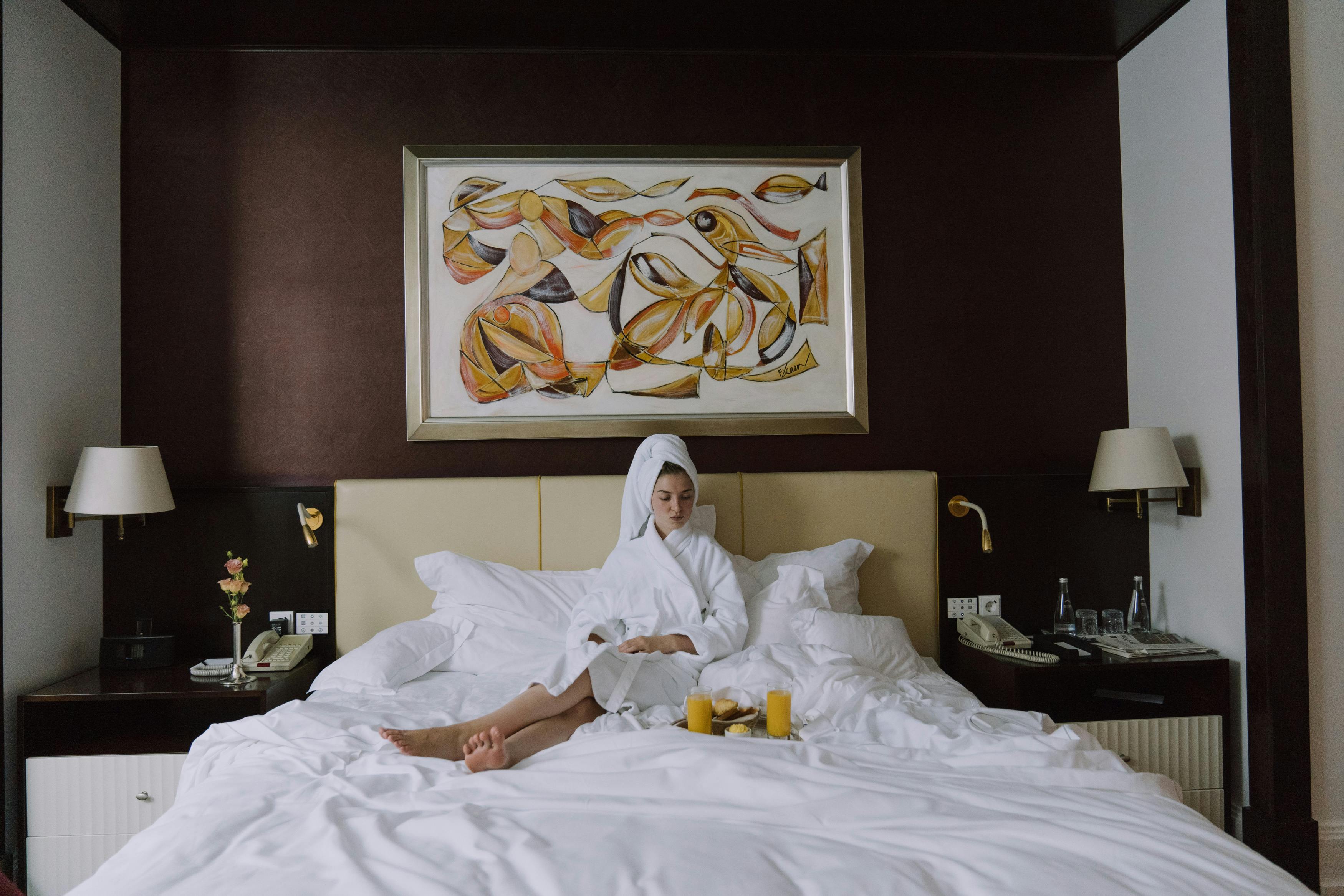 Une femme bouleversée assise sur le lit d'une chambre d'hôtel en peignoir | Source : Pexels