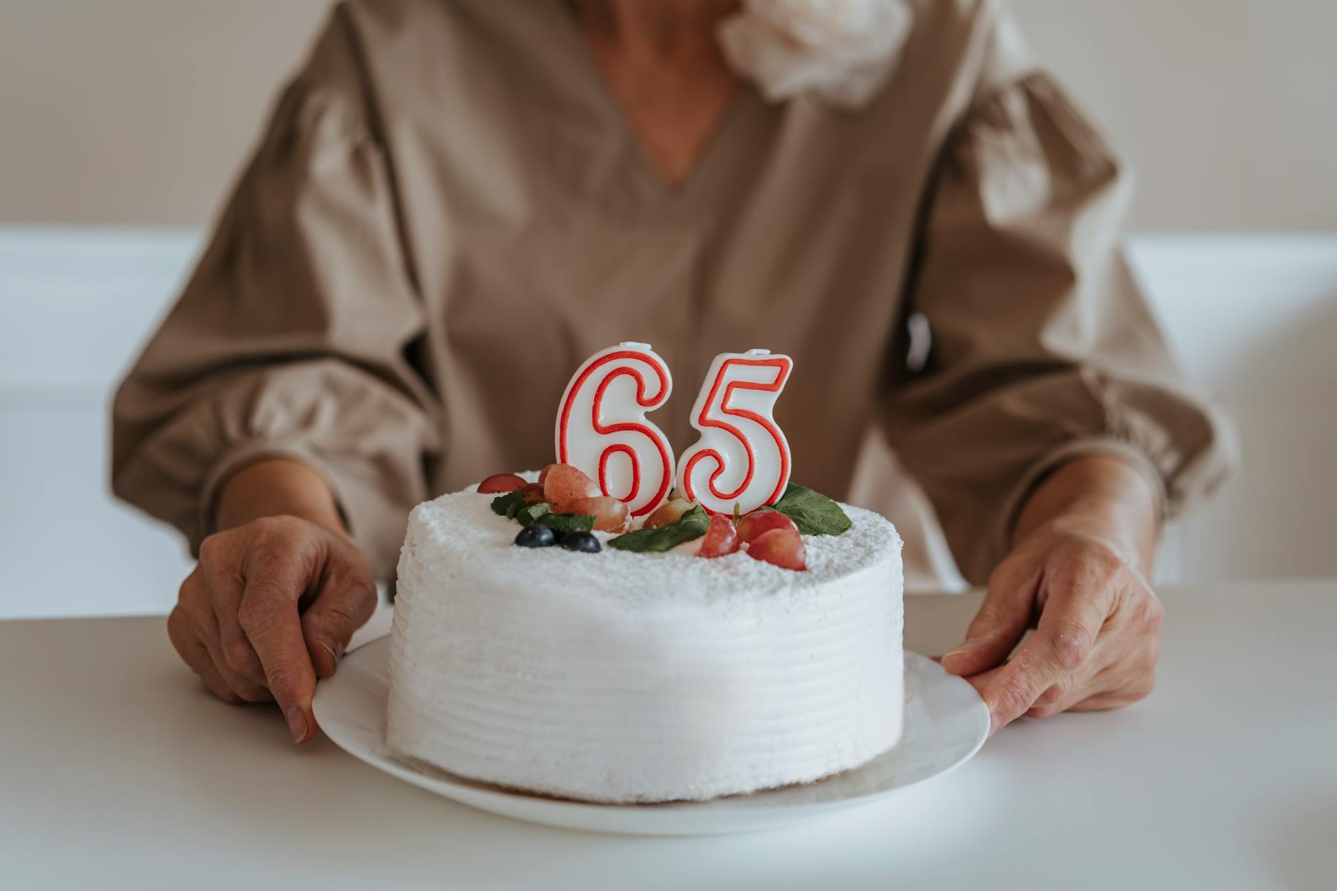 Photo recadrée d'une femme âgée tenant son gâteau d'anniversaire de 65 ans | Source : Pexels