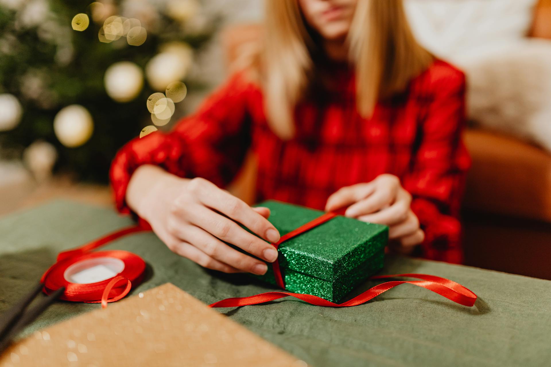 Une femme tenant une boîte verte autour de laquelle est enroulé un ruban rouge | Source : Pexels