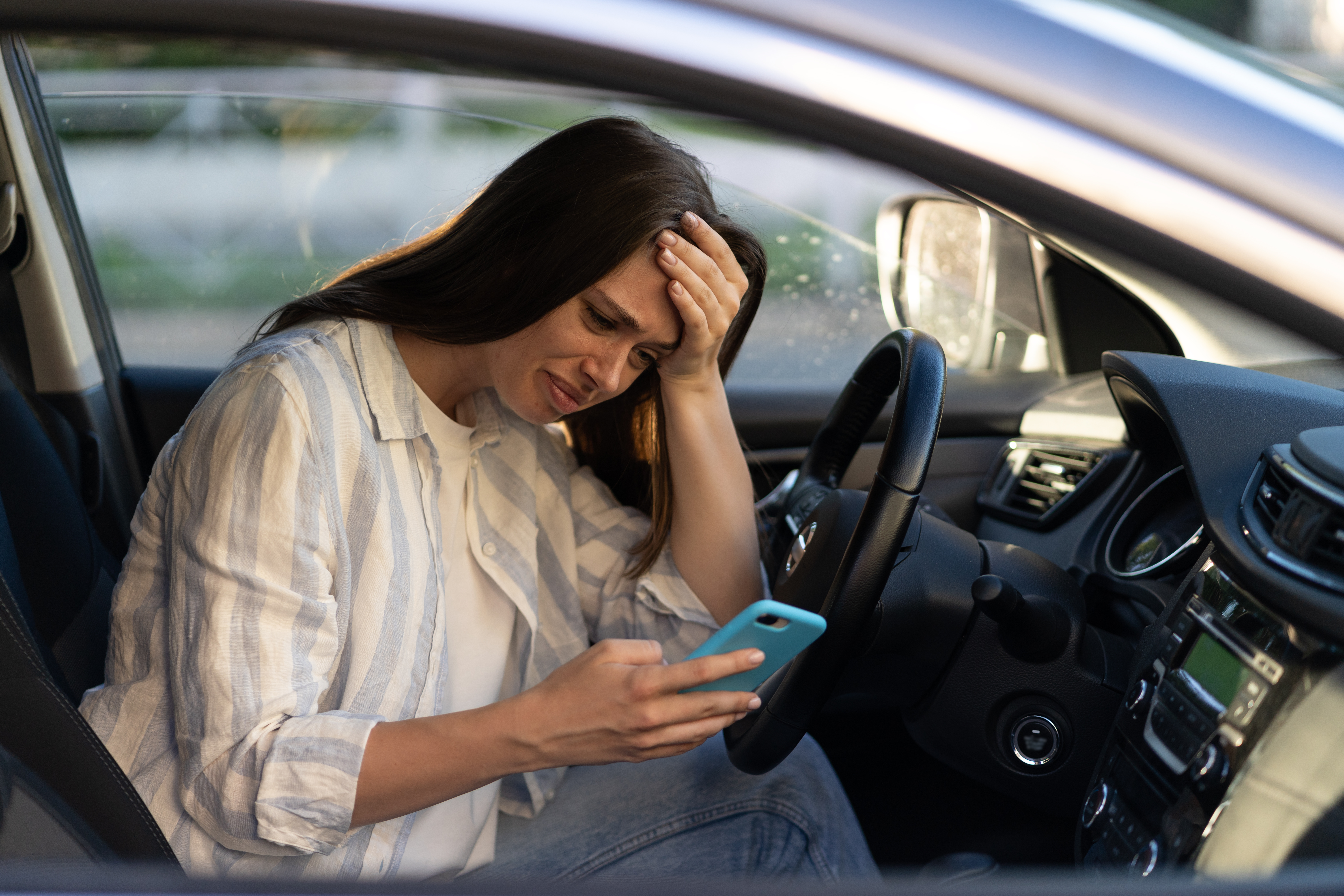Une fille malheureuse pleure en lisant un message sms sur son smartphone au volant d'une voiture. Une femme bouleversée rompt avec son petit ami | Source : Getty Images
