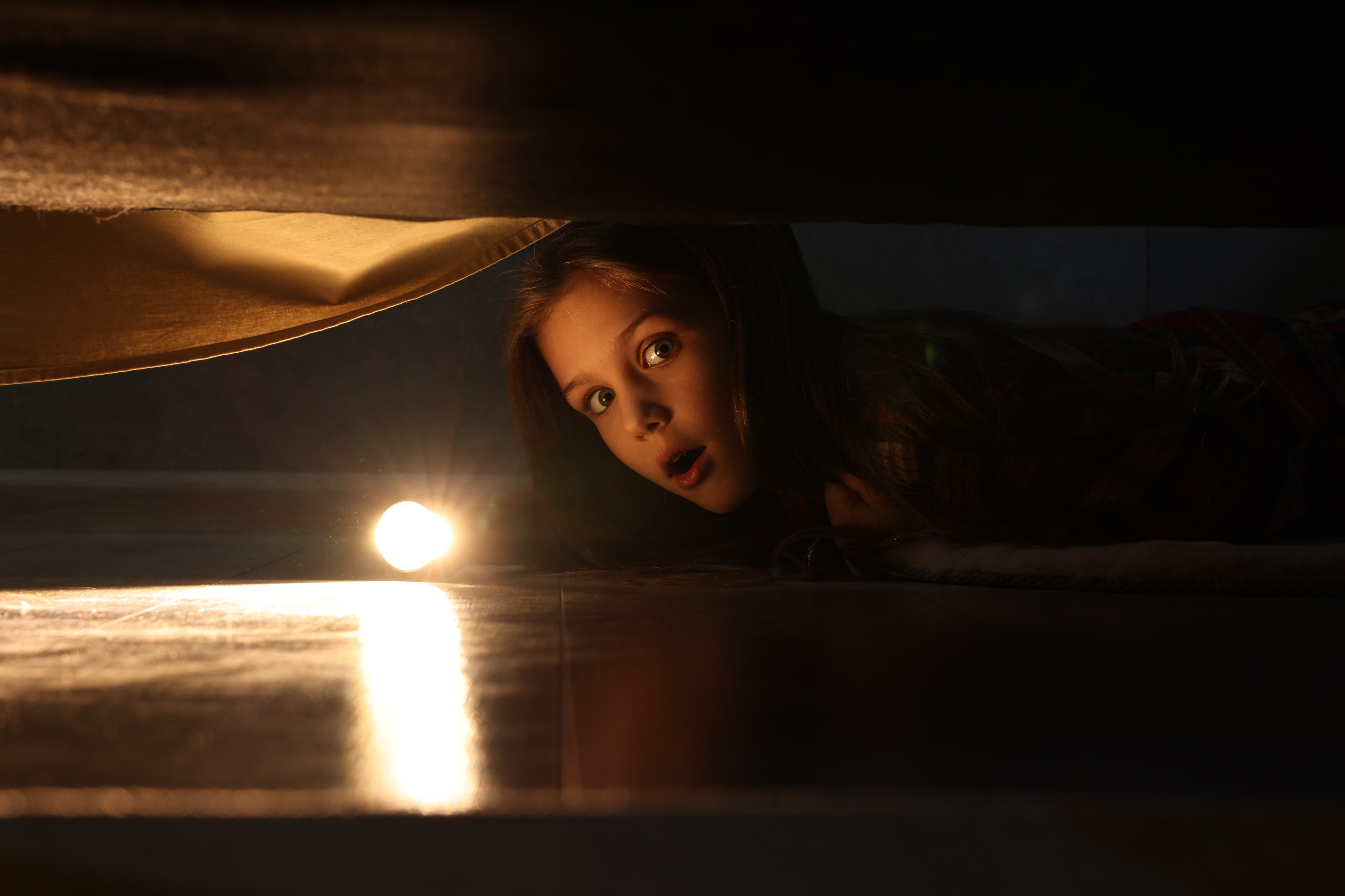 Une fille choquée tenant une lampe de poche et regardant sous le lit | Source : Shutterstock