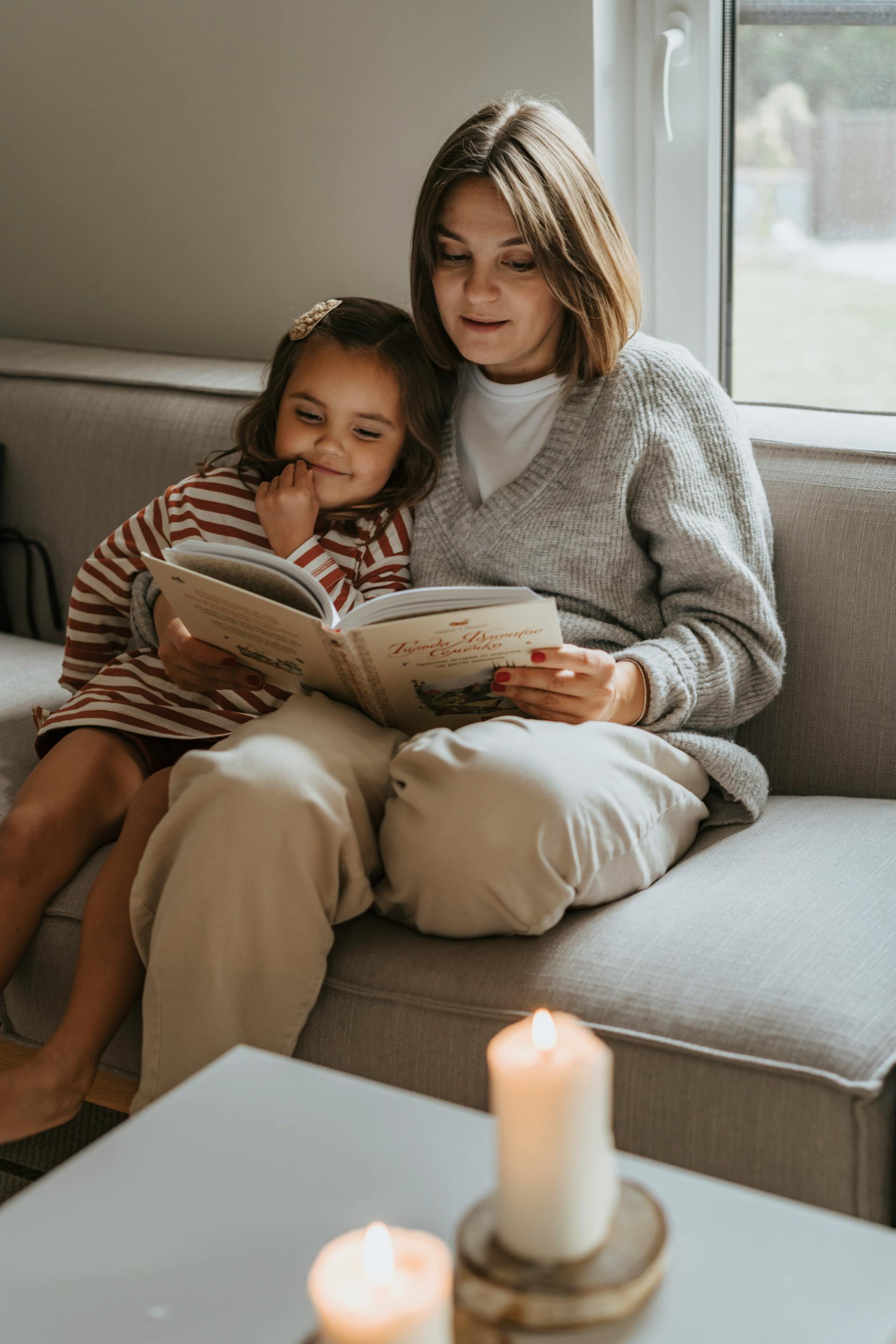 Une femme fait la lecture à une petite fille sur un canapé | Source : Pexels