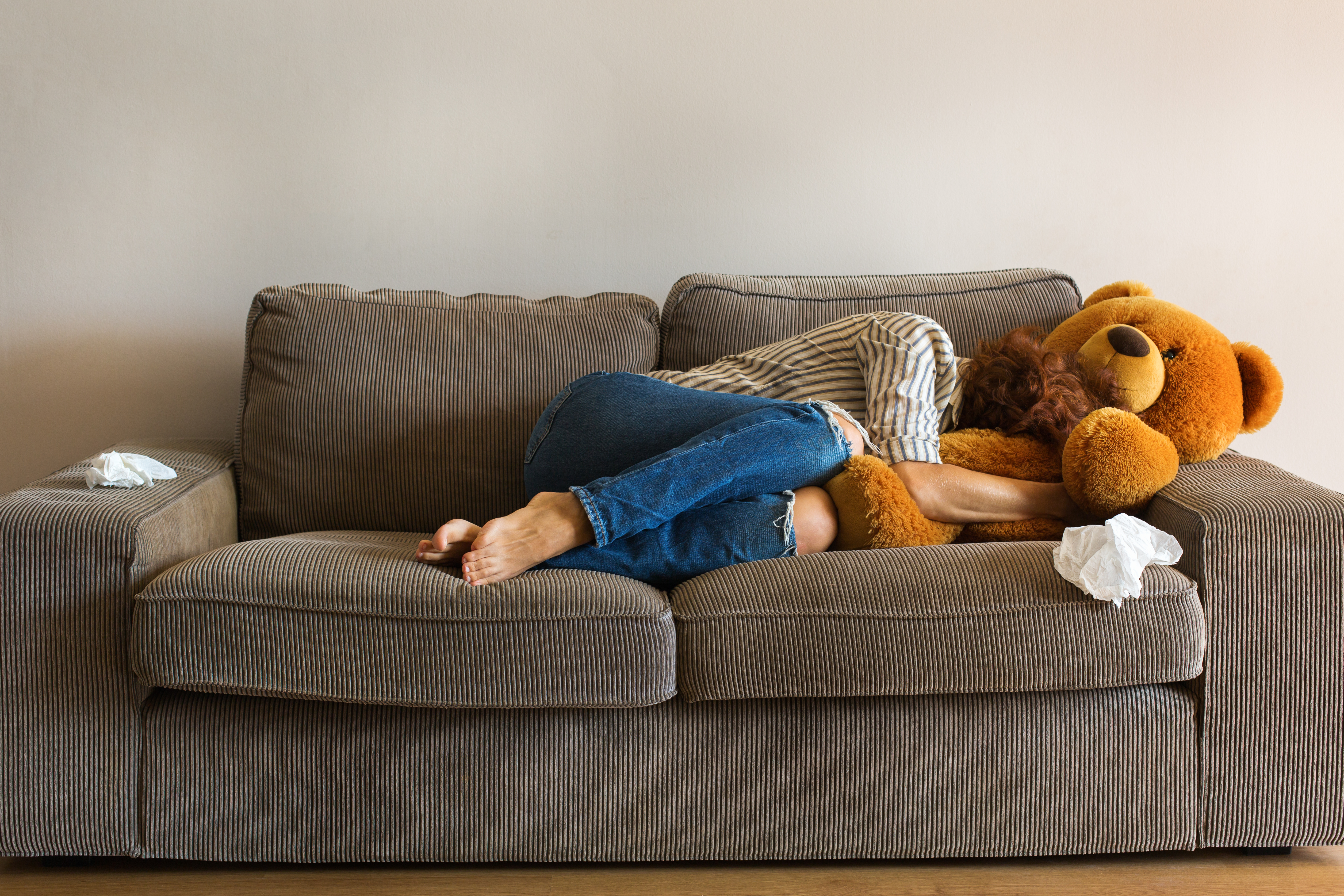 Une jeune femme déprimée s'allonge sur le canapé et pleure en serrant un ours en peluche dans ses bras | Source : Shutterstock