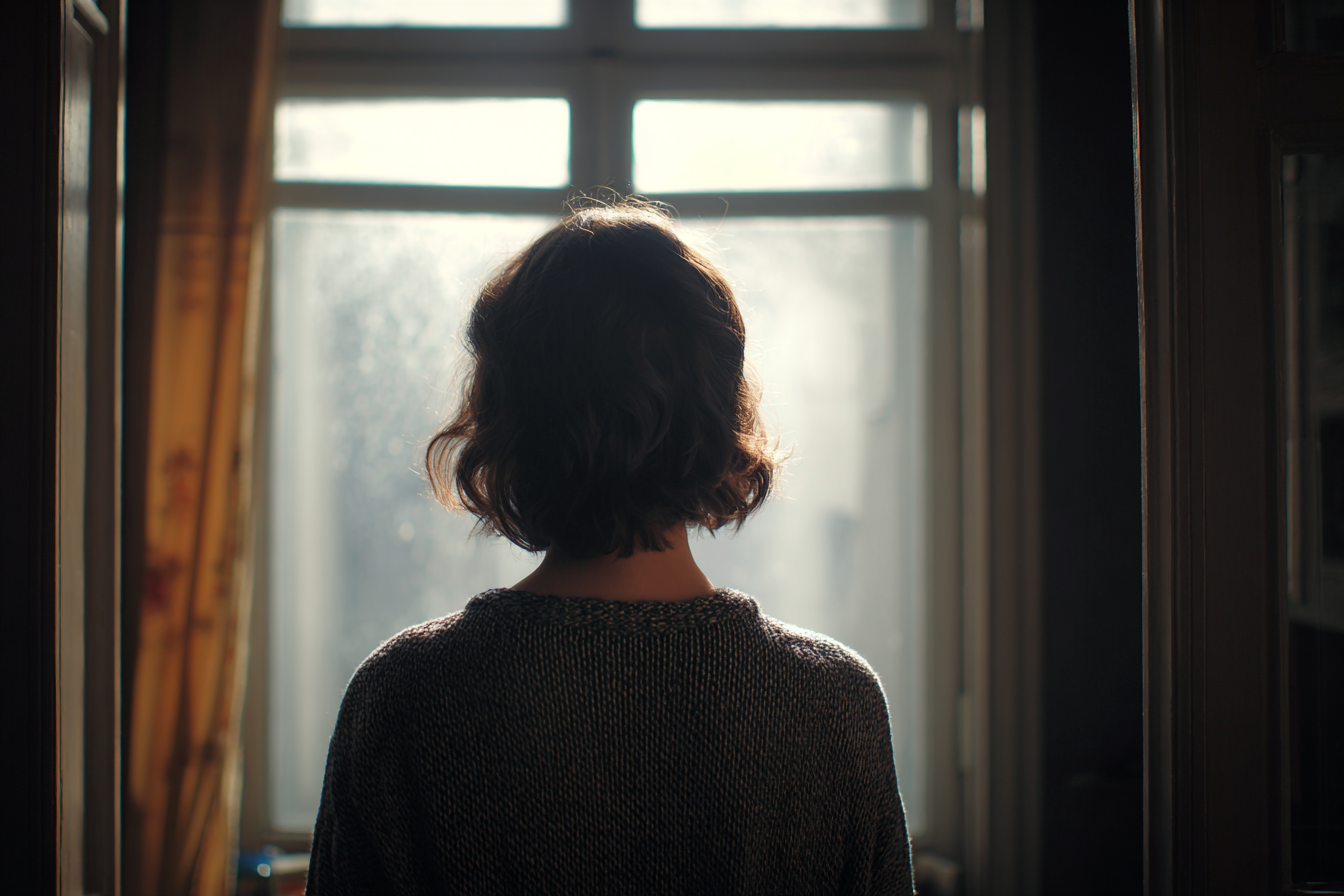 Une femme debout près d'une fenêtre | Source : Midjourney