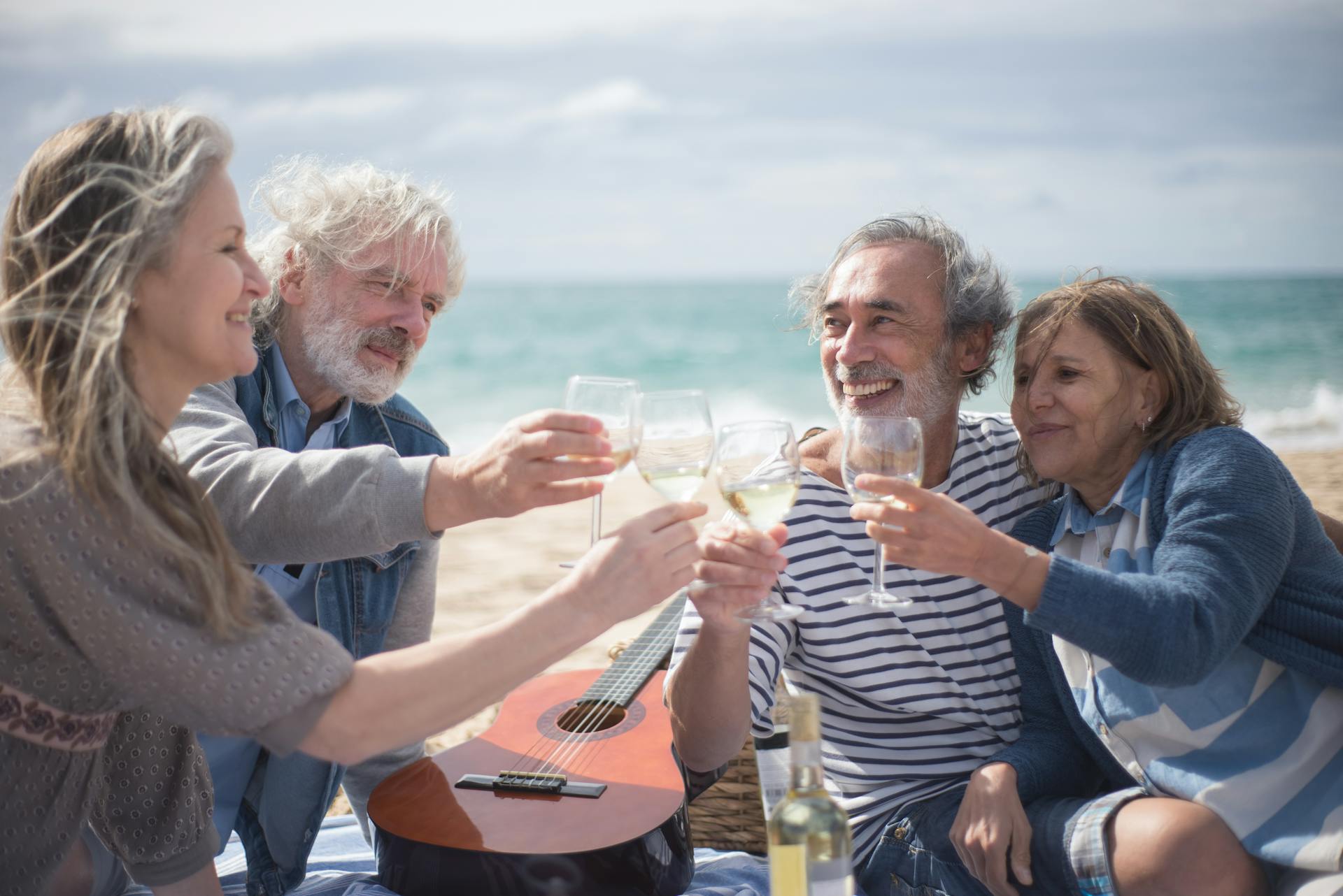 Des personnes aux cheveux gris trinquent avec des verres de vin à la plage | Source : Pexels