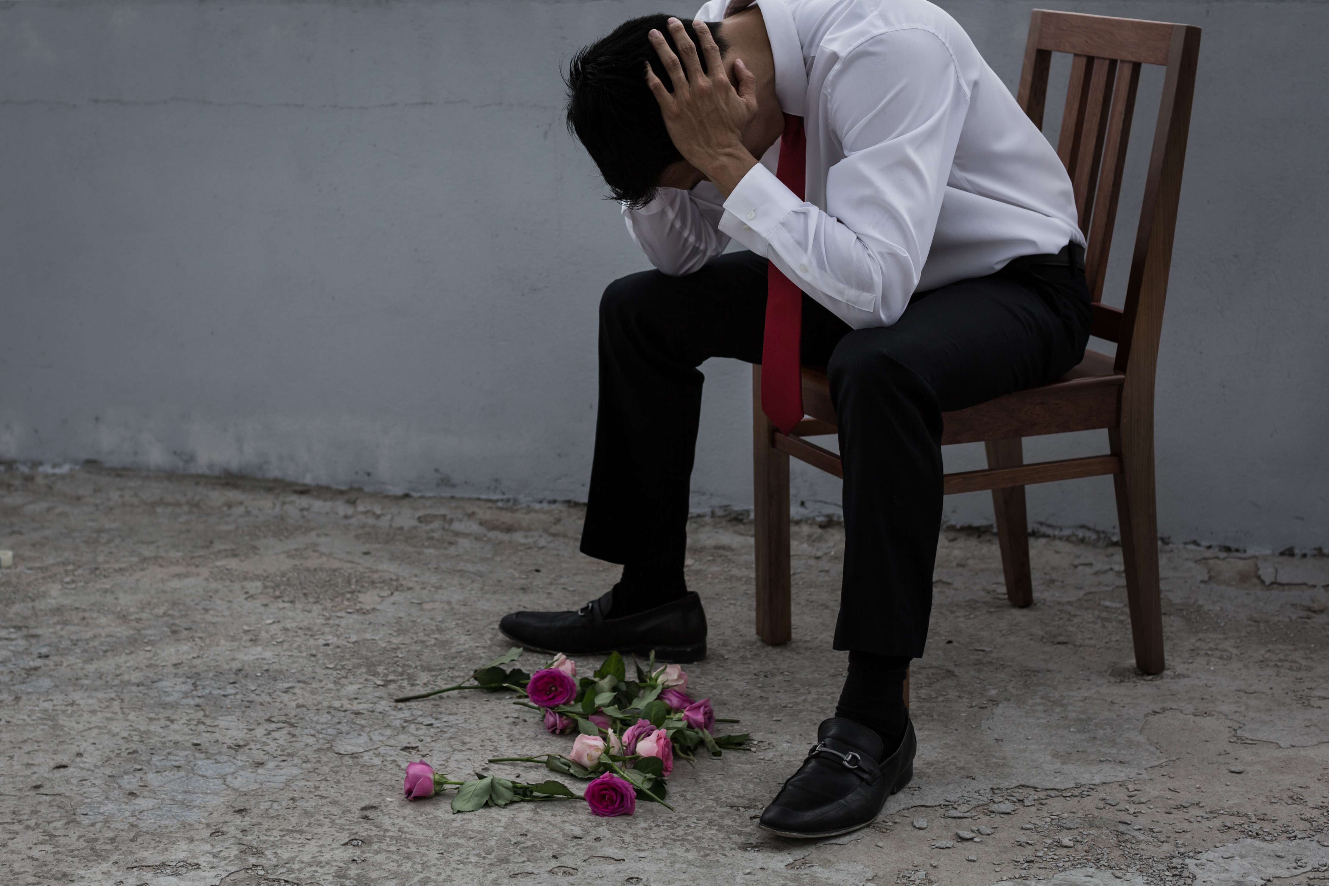 Un homme à l'air triste avec des fleurs éparpillées sur le sol | Source : Shutterstock