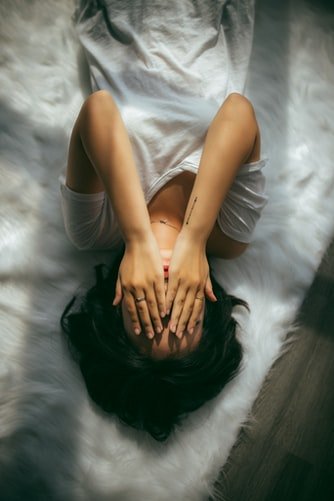 Une femme allongée sur un lit avec la main sur le visage. | Photo : Unsplash