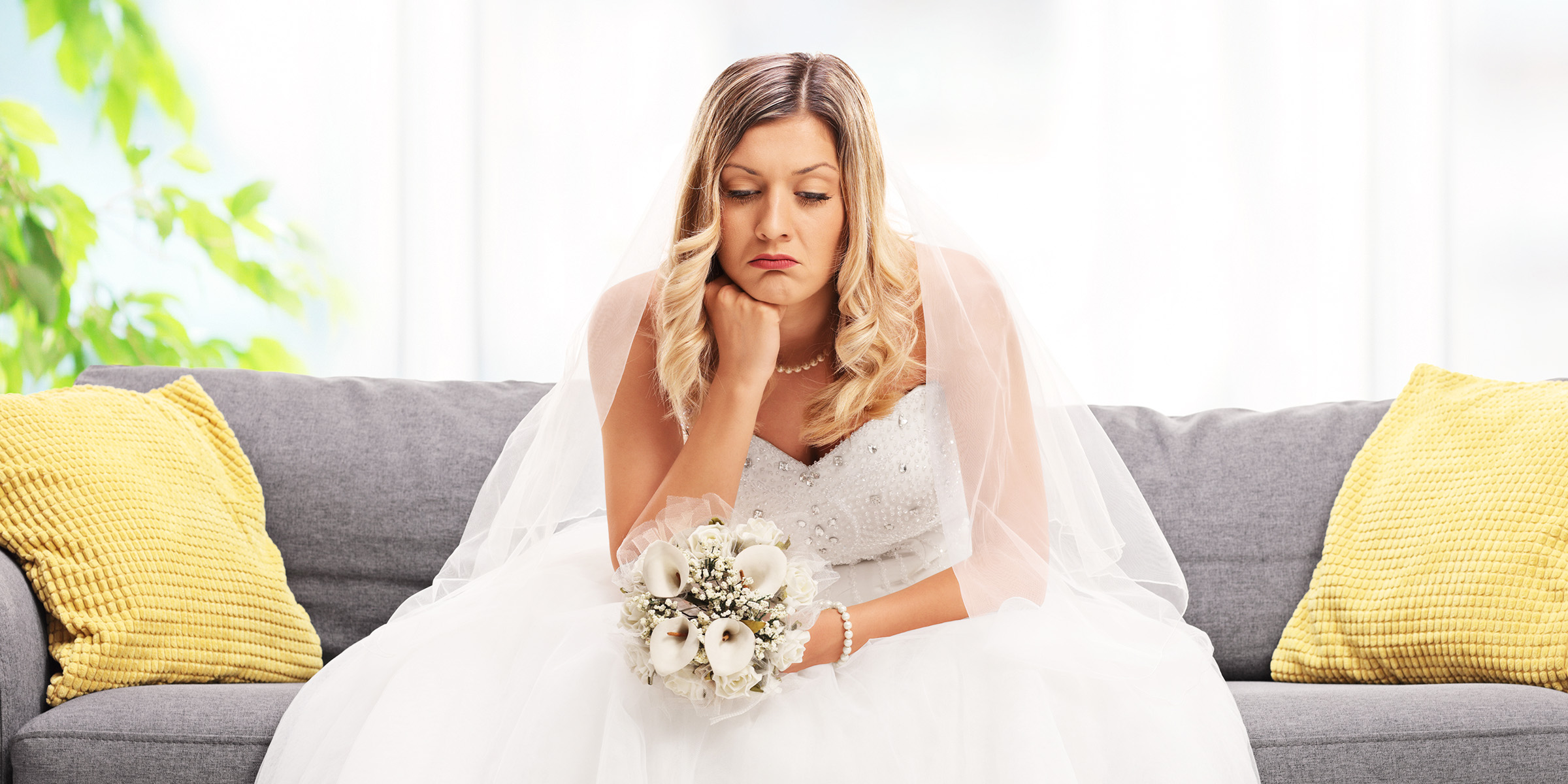 Une mariée assise sur un canapé, l'air triste et plongé dans ses pensées, tenant son bouquet | Source : Shutterstock