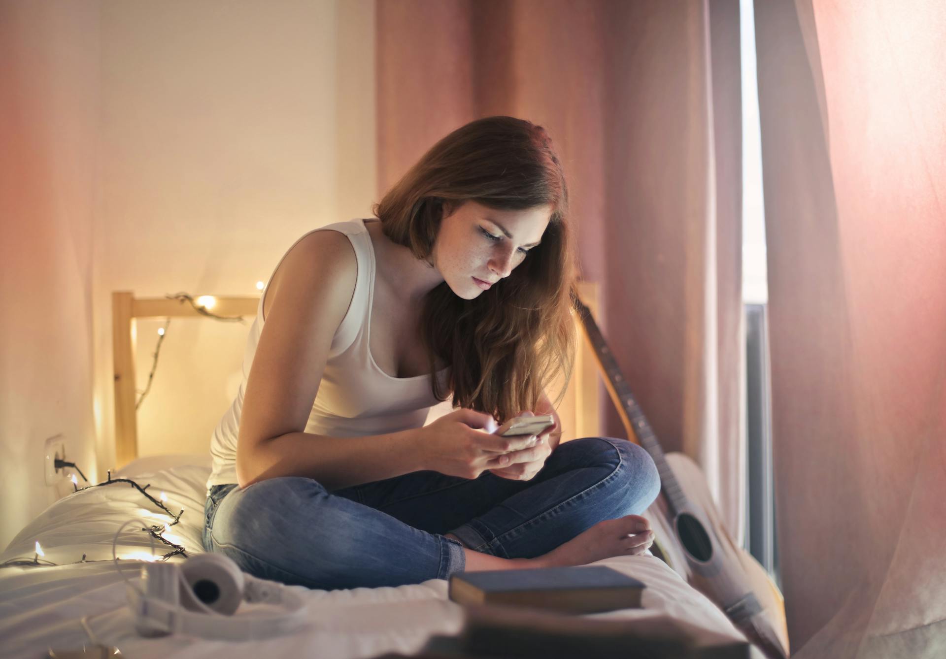 Une femme utilisant son téléphone alors qu'elle est assise sur son lit | Source : Pexels