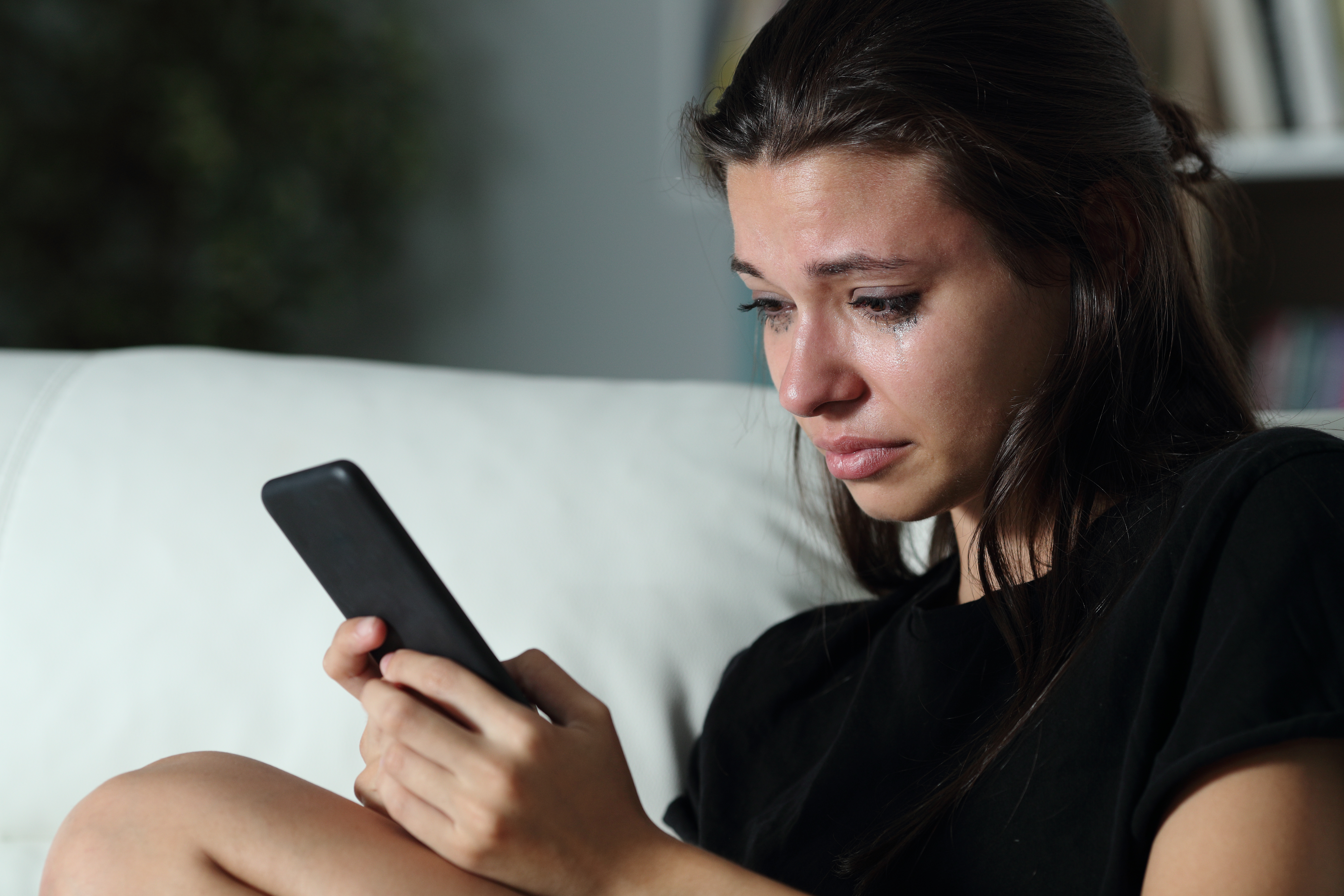 Une jeune fille aux yeux pleins de larmes est photographiée en train de regarder son téléphone portable. | Source : Shutterstock