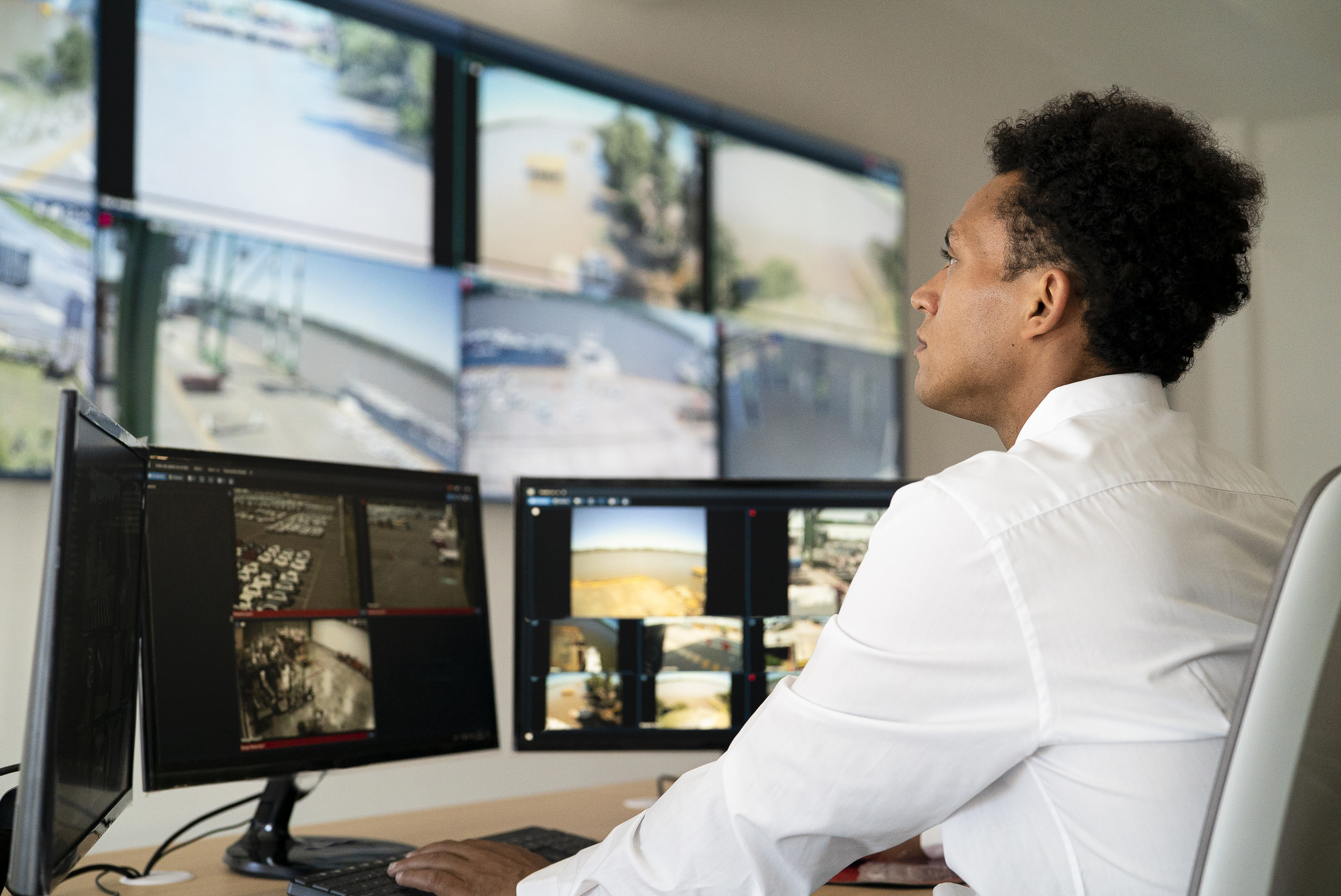 Jeune homme adulte travaillant dans le domaine de la sécurité et regardant un mur vidéo assis à son bureau : Getty Images