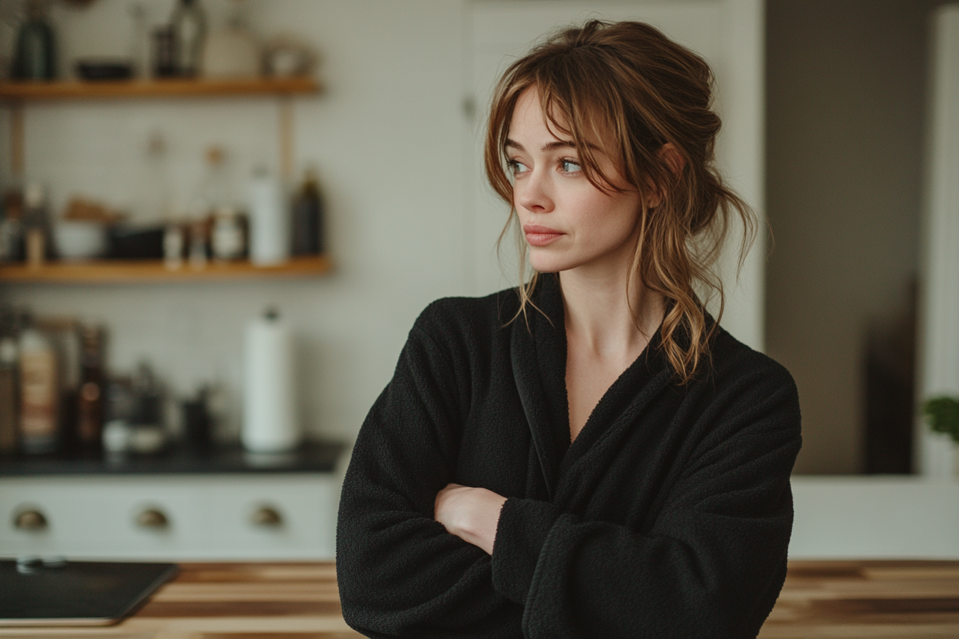 Une femme pensive debout dans une cuisine, les bras croisés | Source : Midjourney