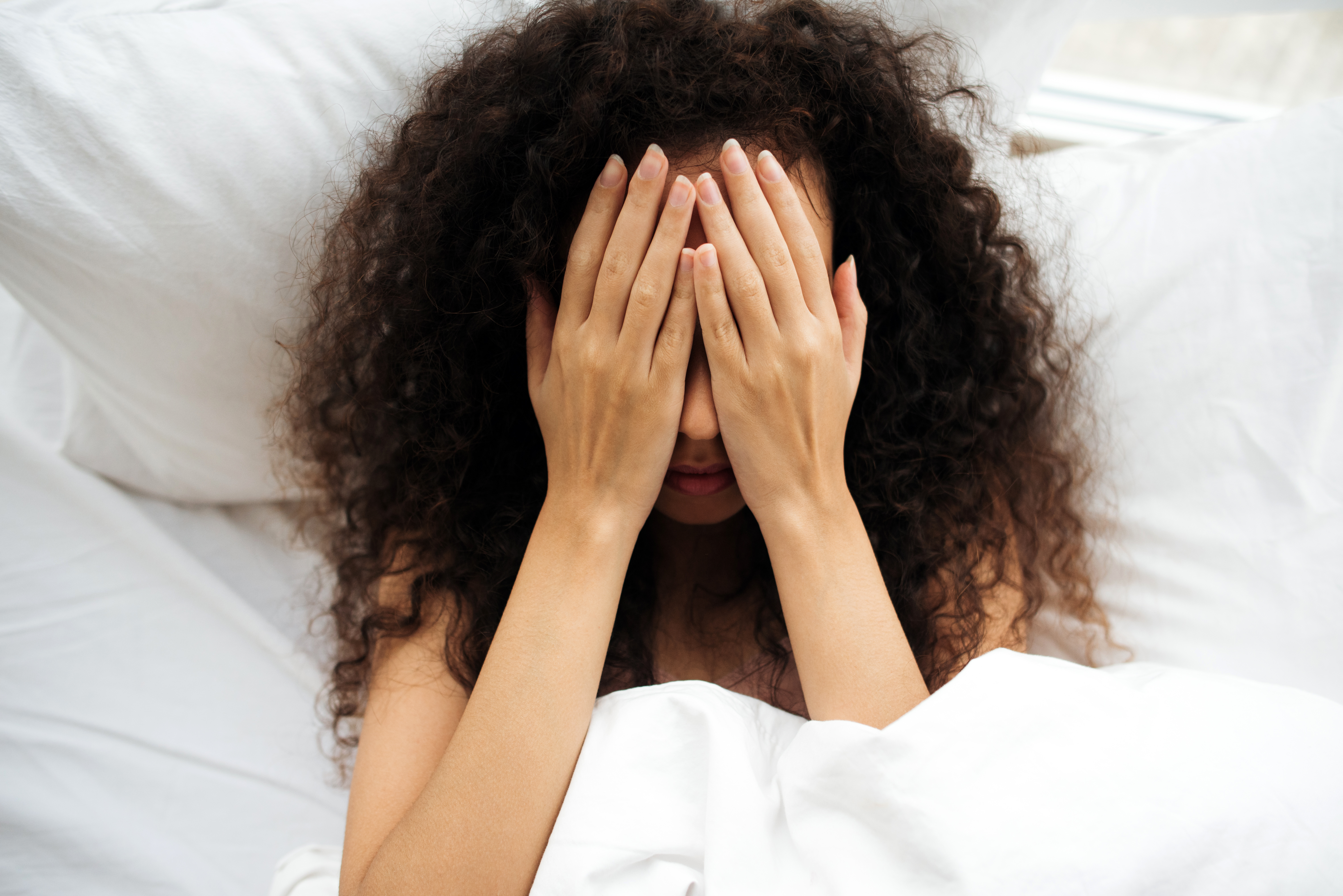 Femme au lit se couvrant le visage avec ses mains | Source : Getty Images