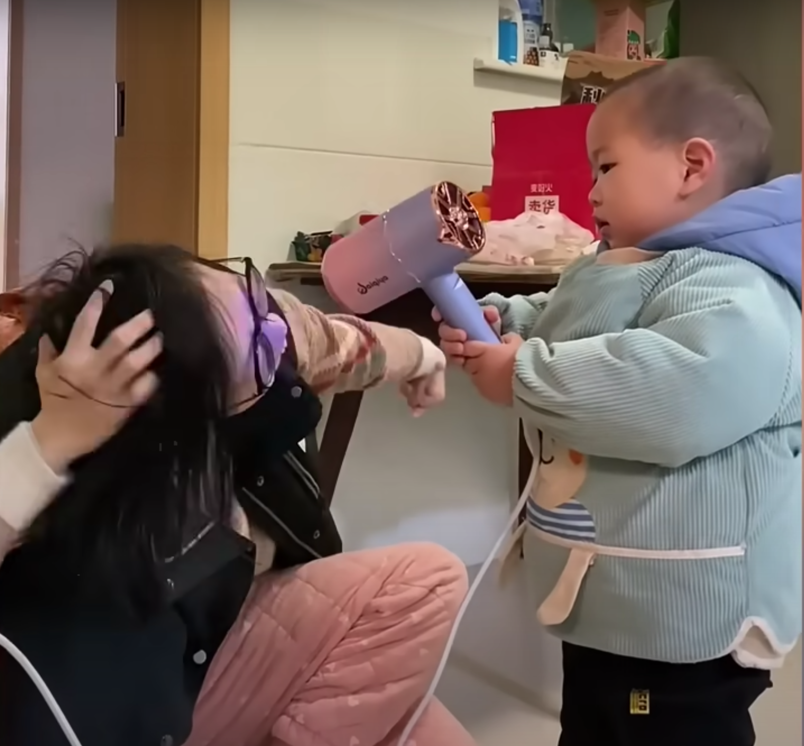 Pomelo aide sa mère à tenir son sèche-cheveux. | Source : Youtube.com/South China Morning Post