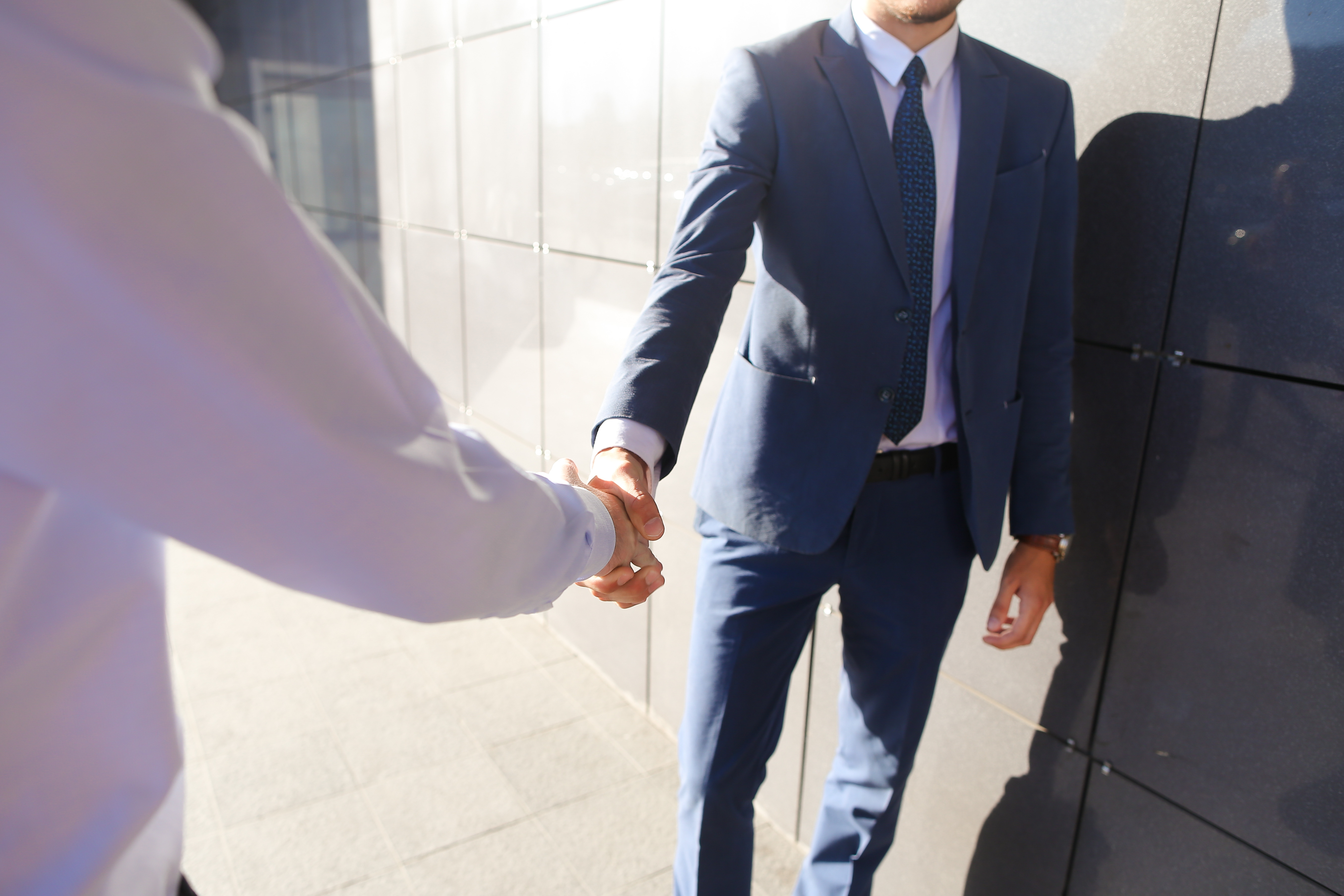 Des amis se sont rencontrés et se saluent en se serrant la main près du mur gris d'un centre d'affaires en plein air. | Source : Shutterstock