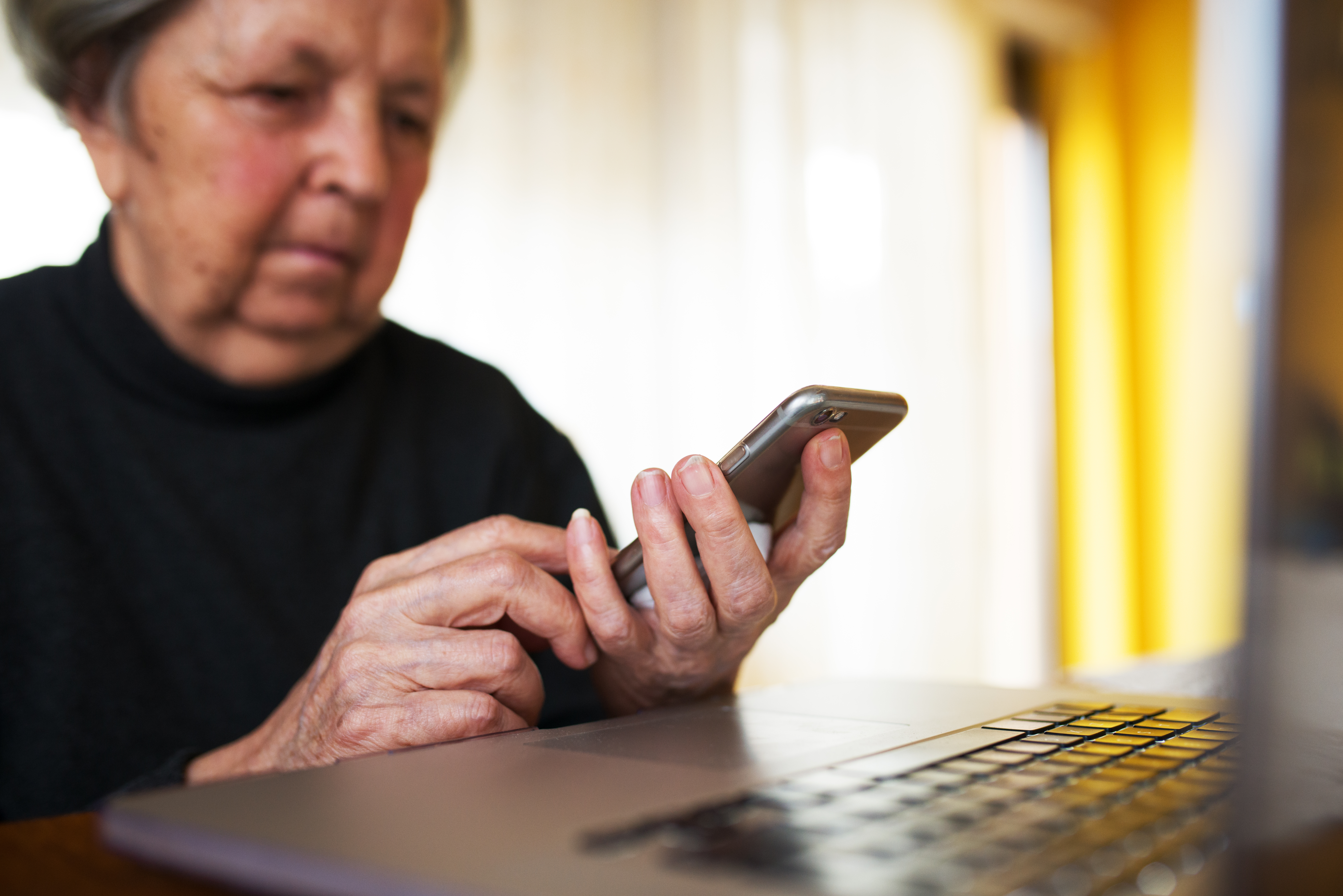 Une femme âgée utilisant un smartphone et un ordinateur portable à la maison | Source : Shutterstock
