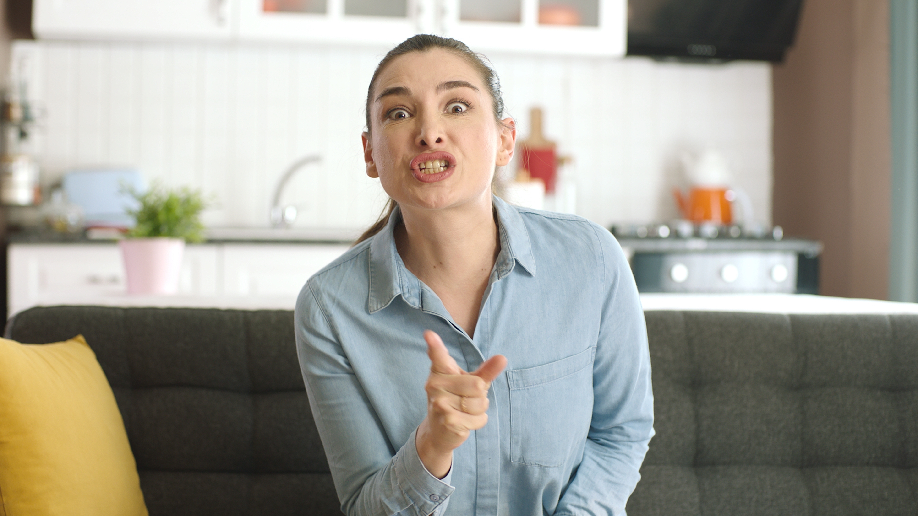 Une femme hystérique assise sur un canapé et pointant du doigt. | Source : Shutterstock