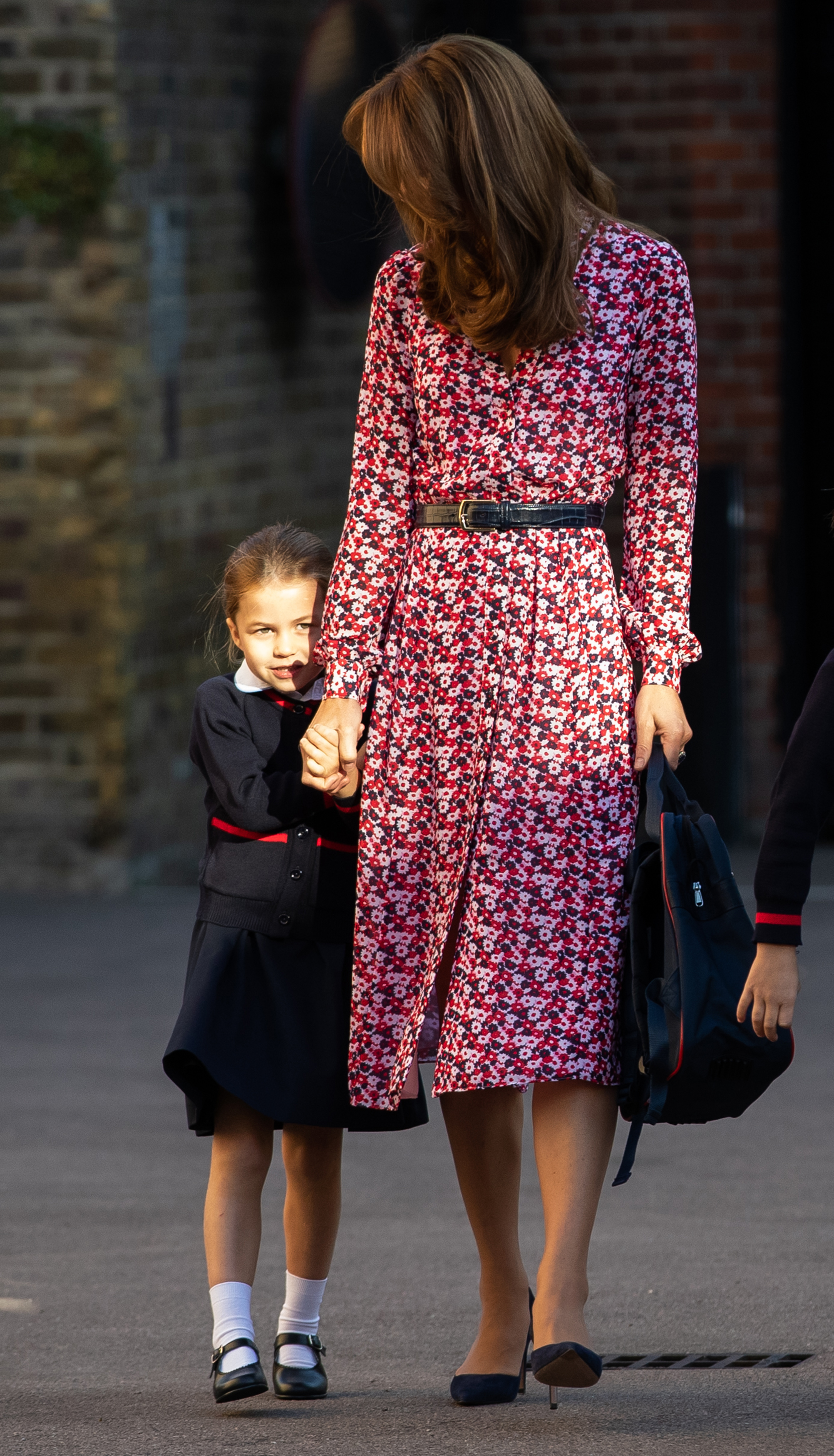 La princesse Charlotte tient la main de sa mère Catherine alors qu'elle arrive pour son tout premier jour d'école à Thomas's Battersea, le 5 septembre 2019, à Londres, en Angleterre. La jeune princesse jette un regard timide vers les passants, vêtue d’une jupe d’uniforme scolaire bleu marine et rouge, d’un cardigan, de chaussettes blanches qui montent jusqu’aux chevilles et de chaussures Mary Jane noires, accompagnée de la duchesse qui porte une robe midi à fleurs rose et bleu marine ceinturée et des escarpins pointus bleu marine. | Source : Getty Images