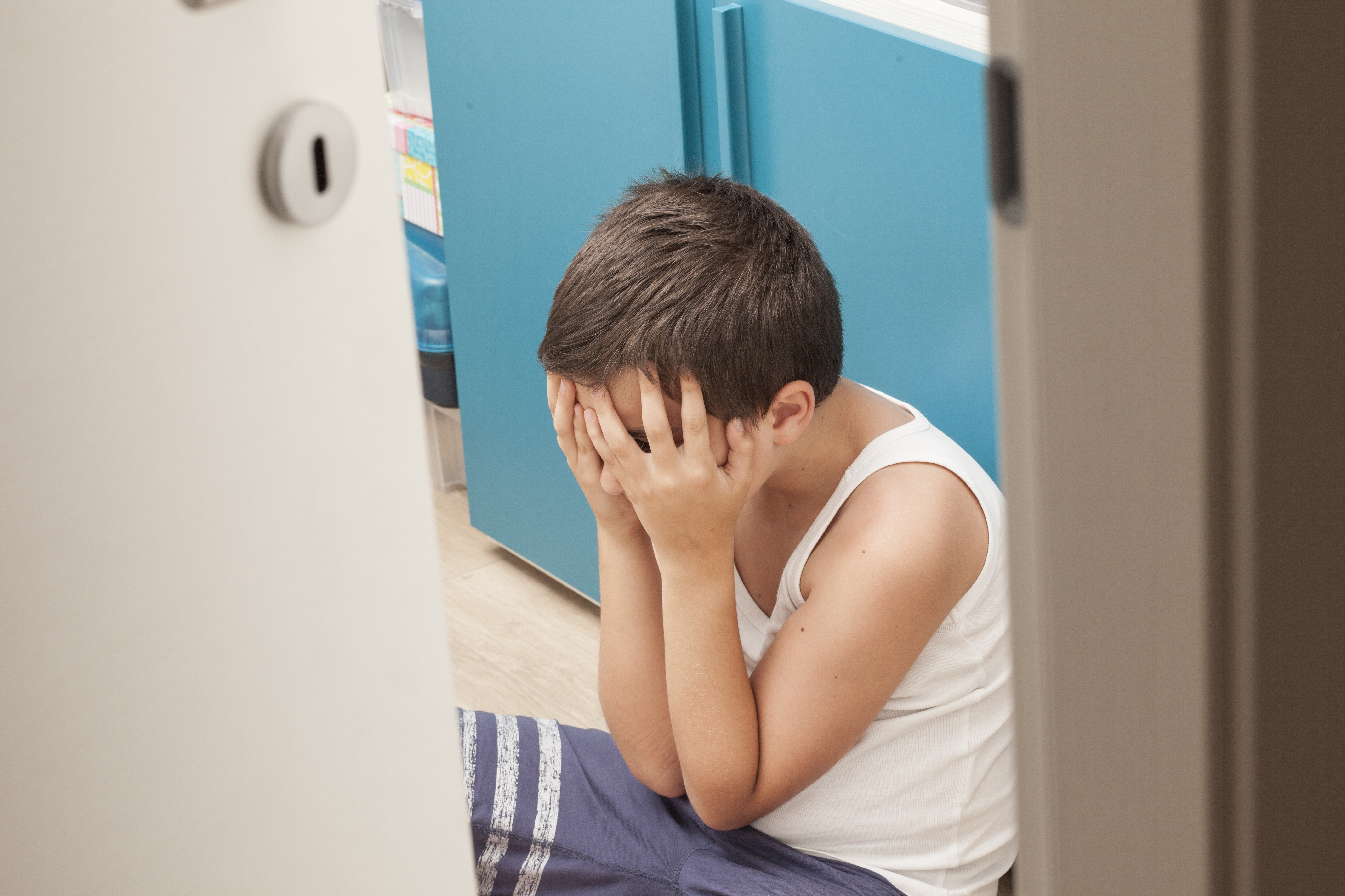 Un jeune garçon se couvrant le visage sur le sol. | Source : Shutterstock