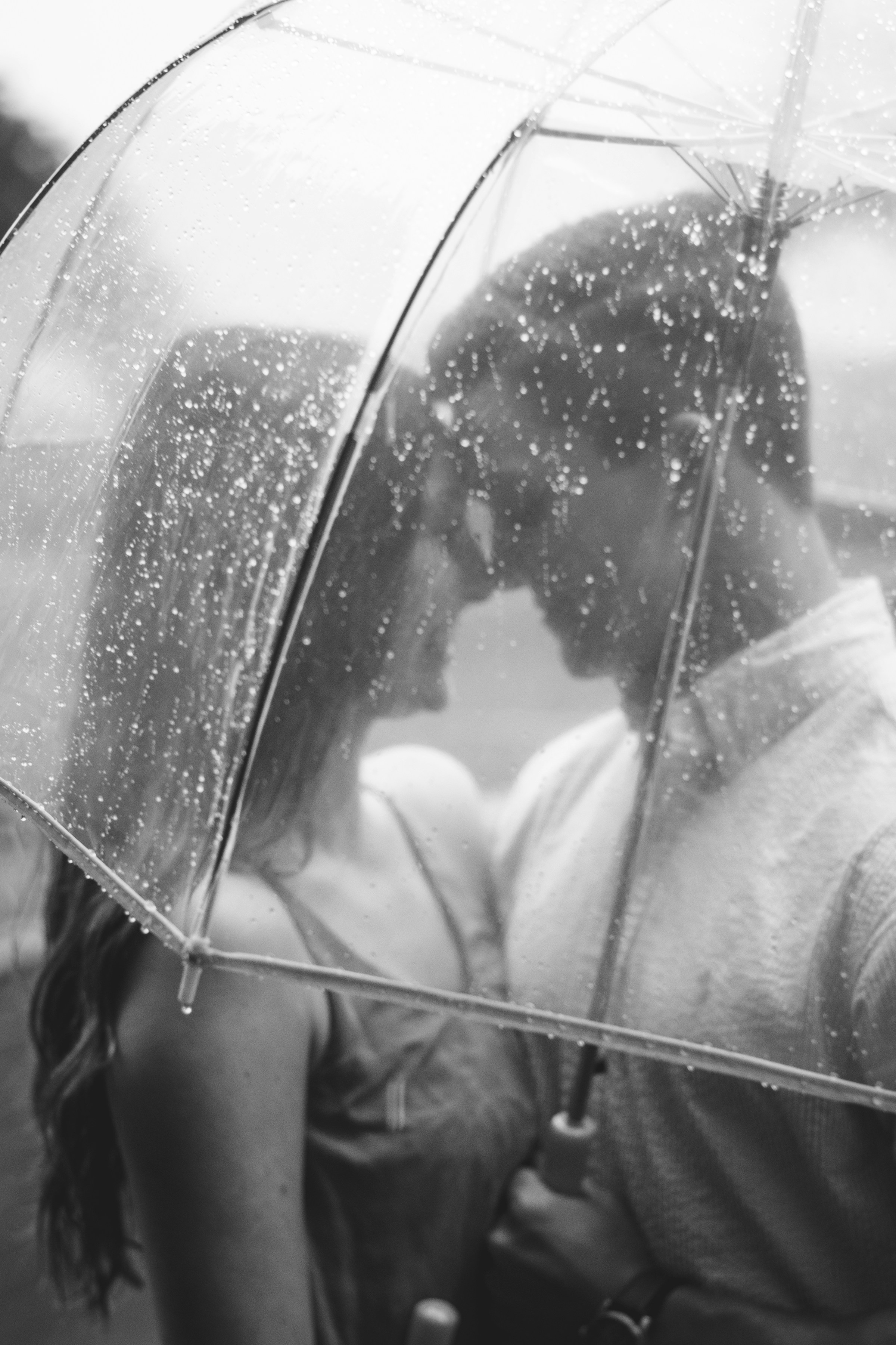 Un jeune couple romantique sous un parapluie transparent un jour de pluie | Source : Unsplash