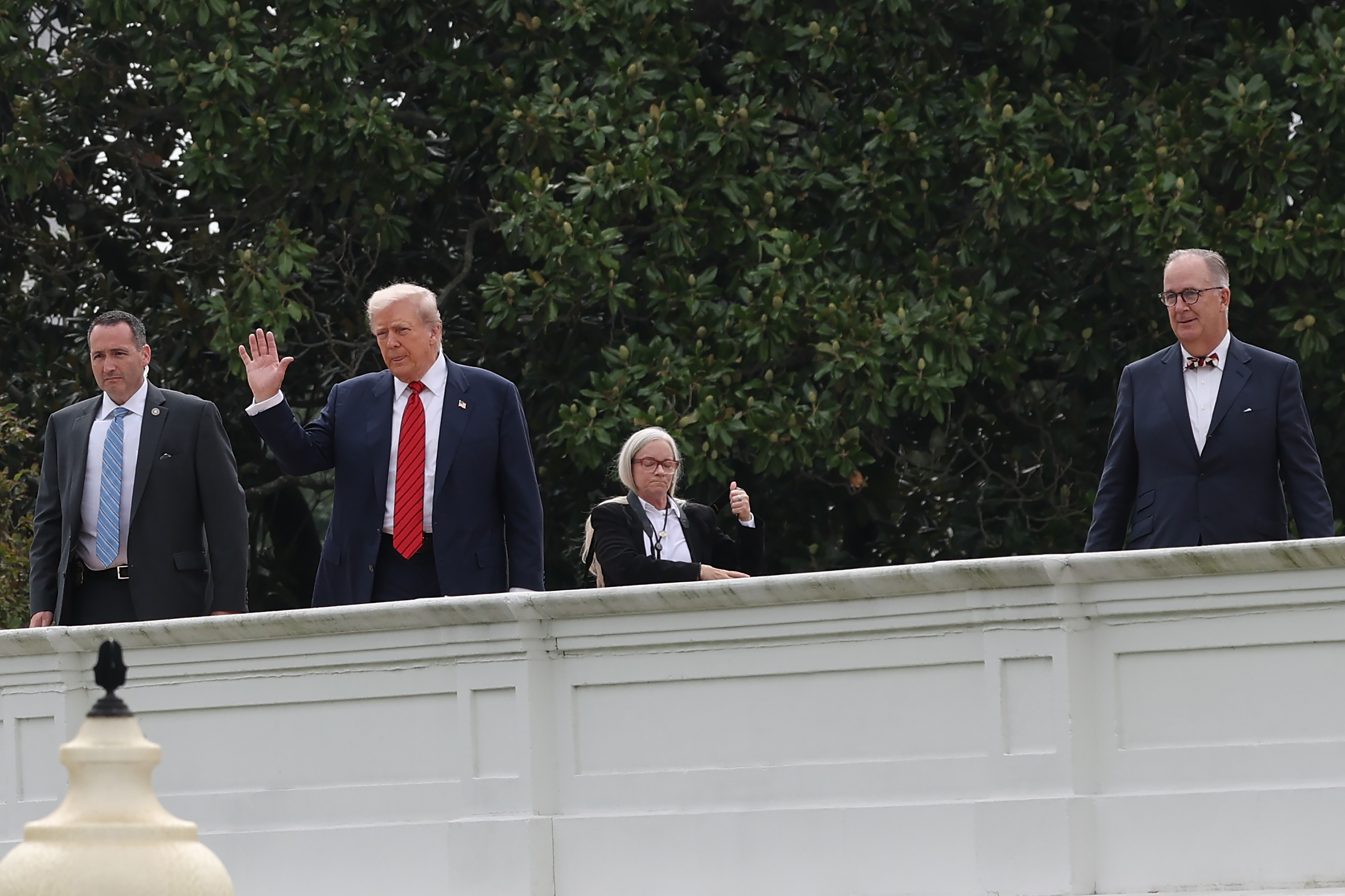 Saluant les journalistes depuis le toit, le président Donald Trump se tient aux côtés de l'architecte James C. McCrery et du personnel de sécurité lors de sa surprenante promenade au sommet de la résidence présidentielle.