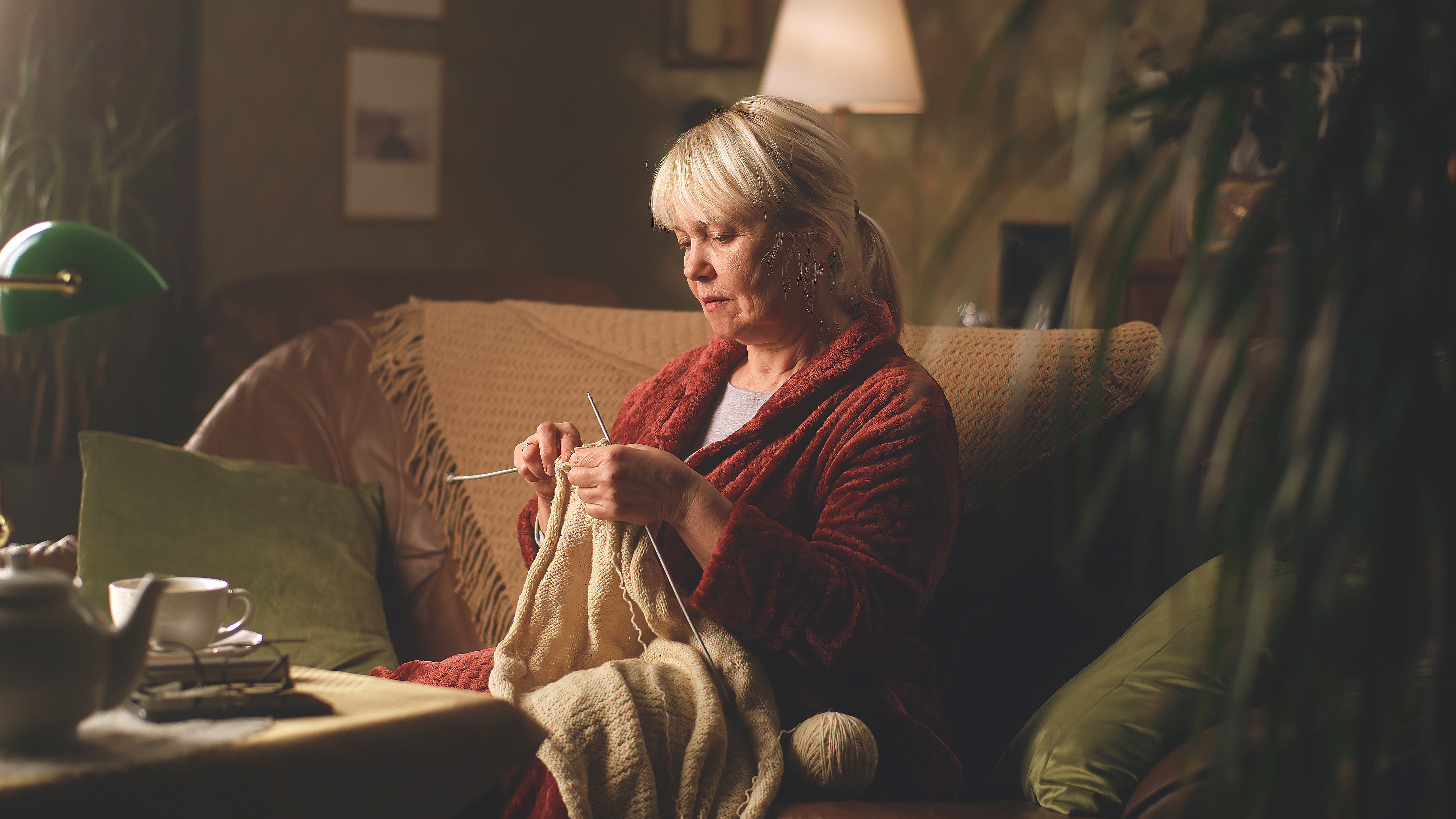 Une femme âgée tricote un pull tout en étant assise sur le canapé | Source : Shutterstock