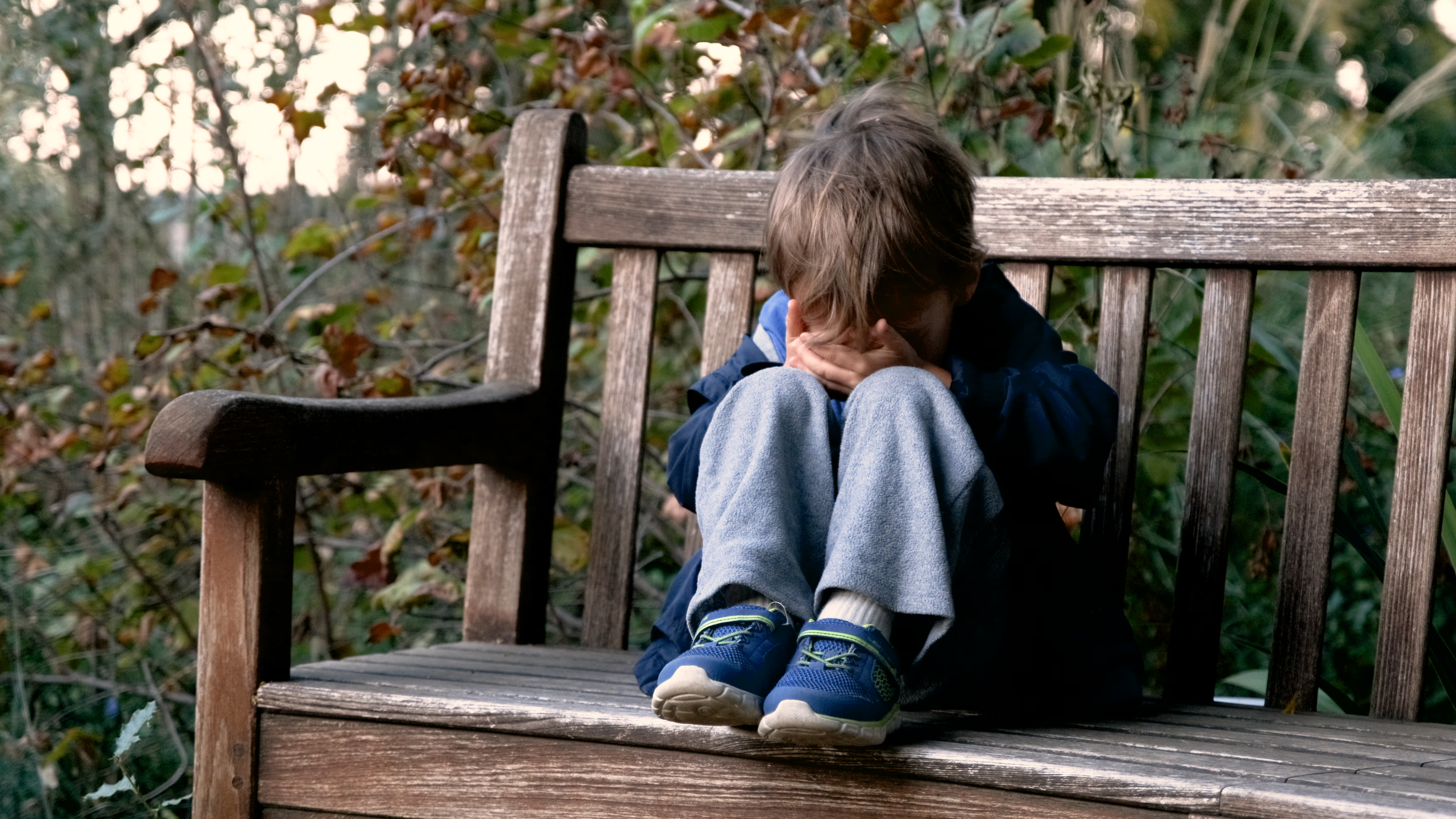 Un petit garçon en pleurs, assis sur un banc dans la cour de récréation, se couvrant le visage I Photo d'illustration I Source : Getty Images