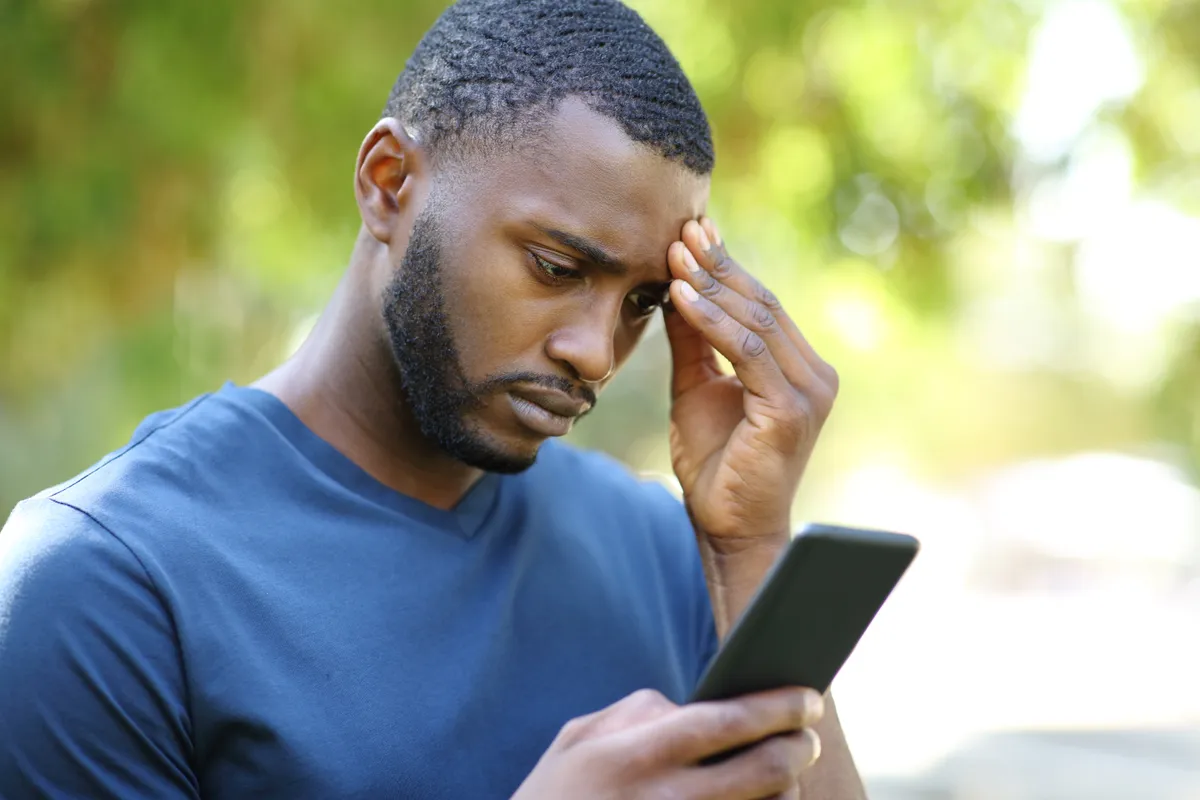 Un homme noir anxieux vérifie son smartphone dans un parc | Source : Getty Images