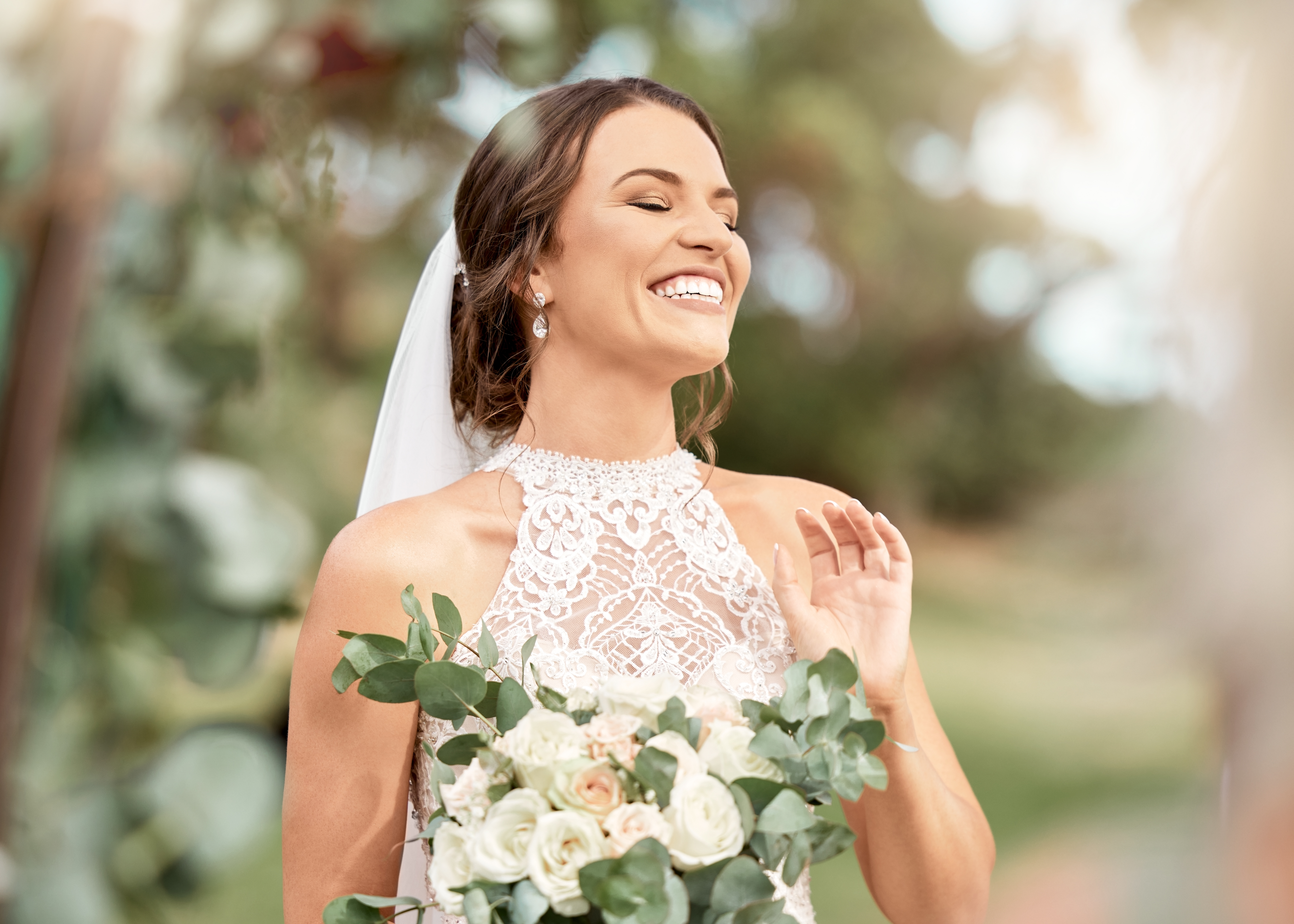 Mariée excitée dans le mariage avec un bouquet dans un parc naturel avec des arbres verts, bokeh et soleil d'été. Bonheur, engagement et rêve d'une femme de beauté avec des fleurs pour le mariage en extérieur lens flare | Source : Getty Images