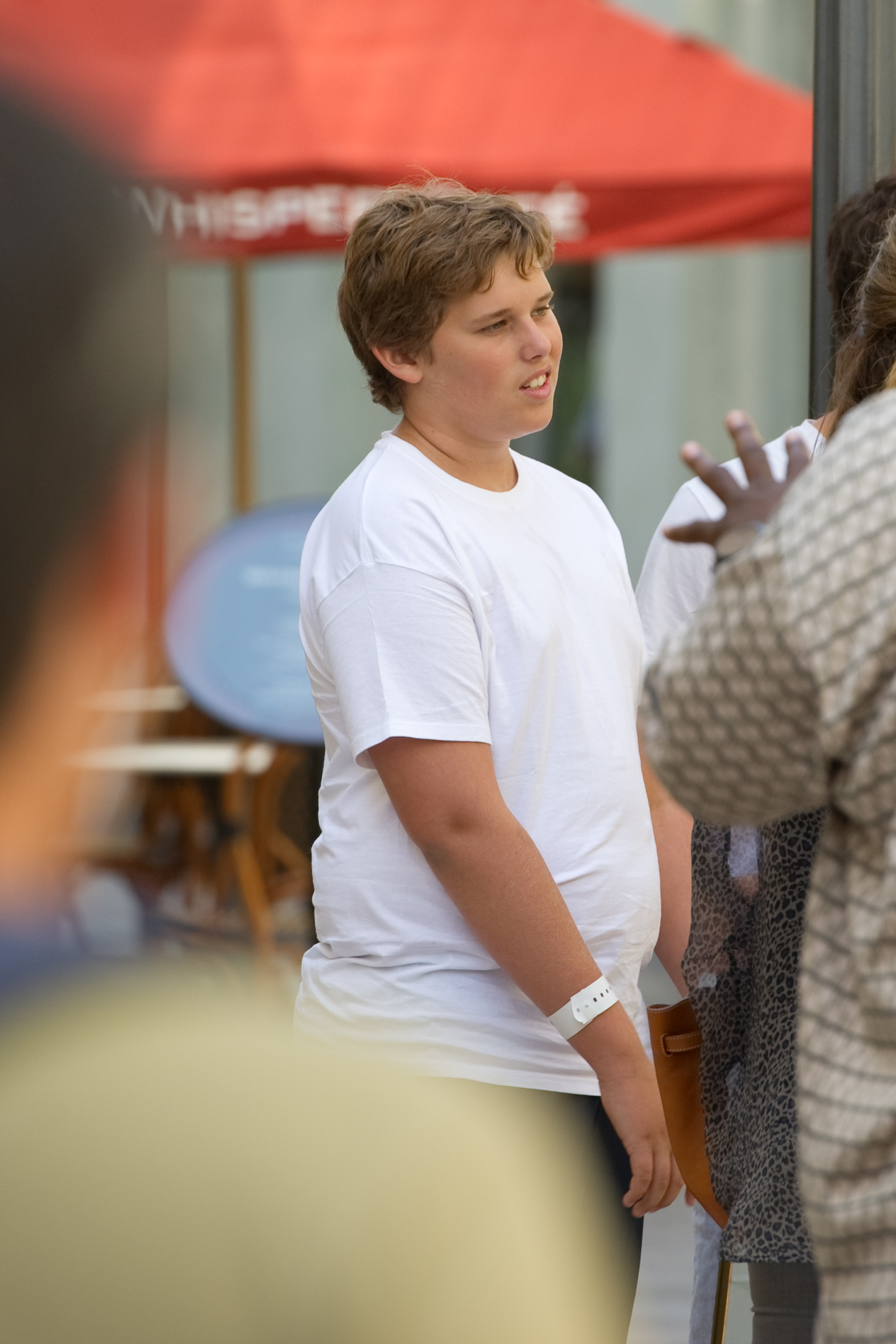 Également prise à The Grove le même jour, cette photo capture Christopher en train d'écouter attentivement une conversation. Son visage juvénile et ses cheveux courts et ébouriffés encadrent son expression, tandis qu'un bracelet blanc est visible sur son poignet gauche.