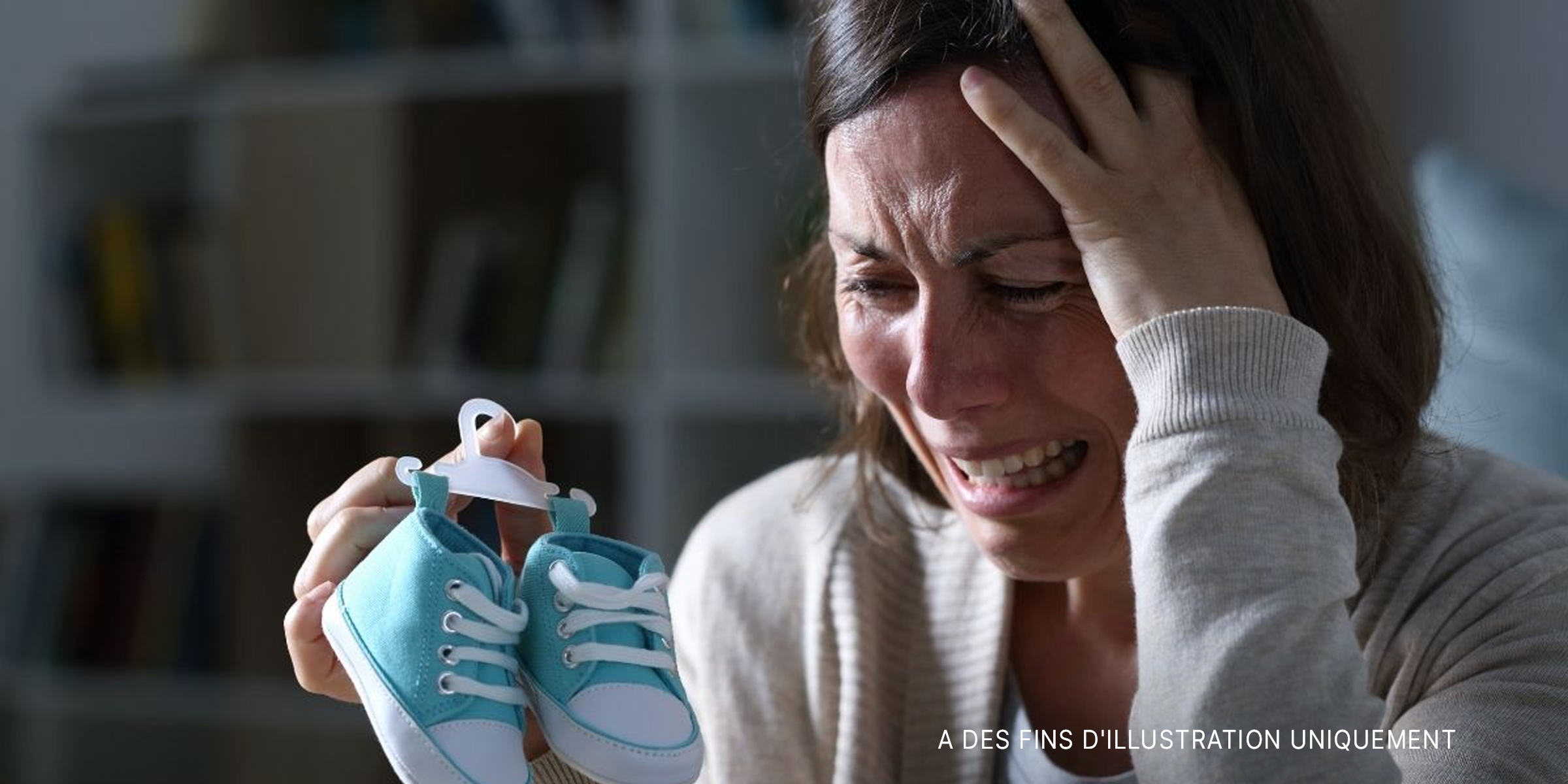 Une femme pleurant en tenant des chaussures de bébé | Source : Shutterstock